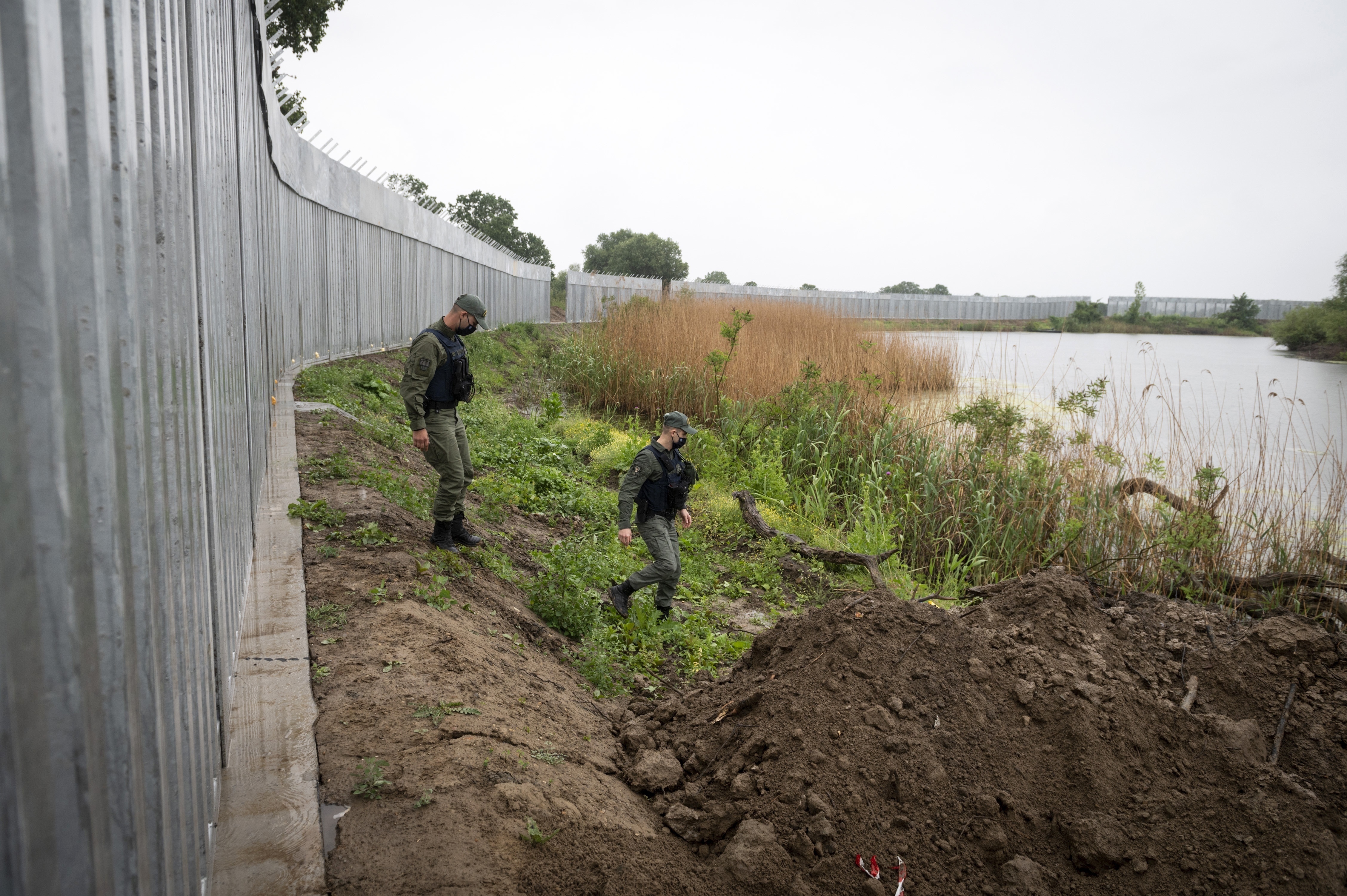 Greek policemen patrol alongside a steel wall at Evros river