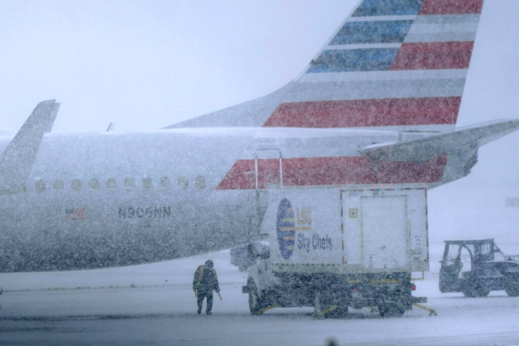Snow falls on a ground crew working outside a parked plane at Dallas Fort Worth International Airport .