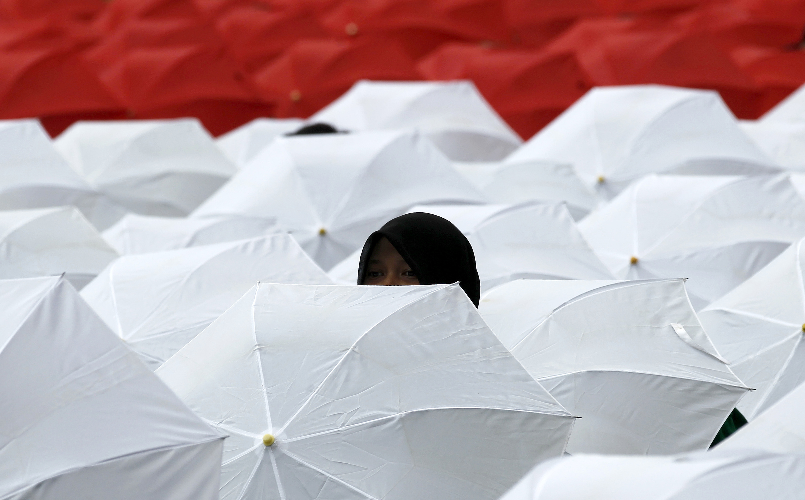 A woman peeks out from a sea of white and red umbrellas opened to create the Indonesian flag by members of NU