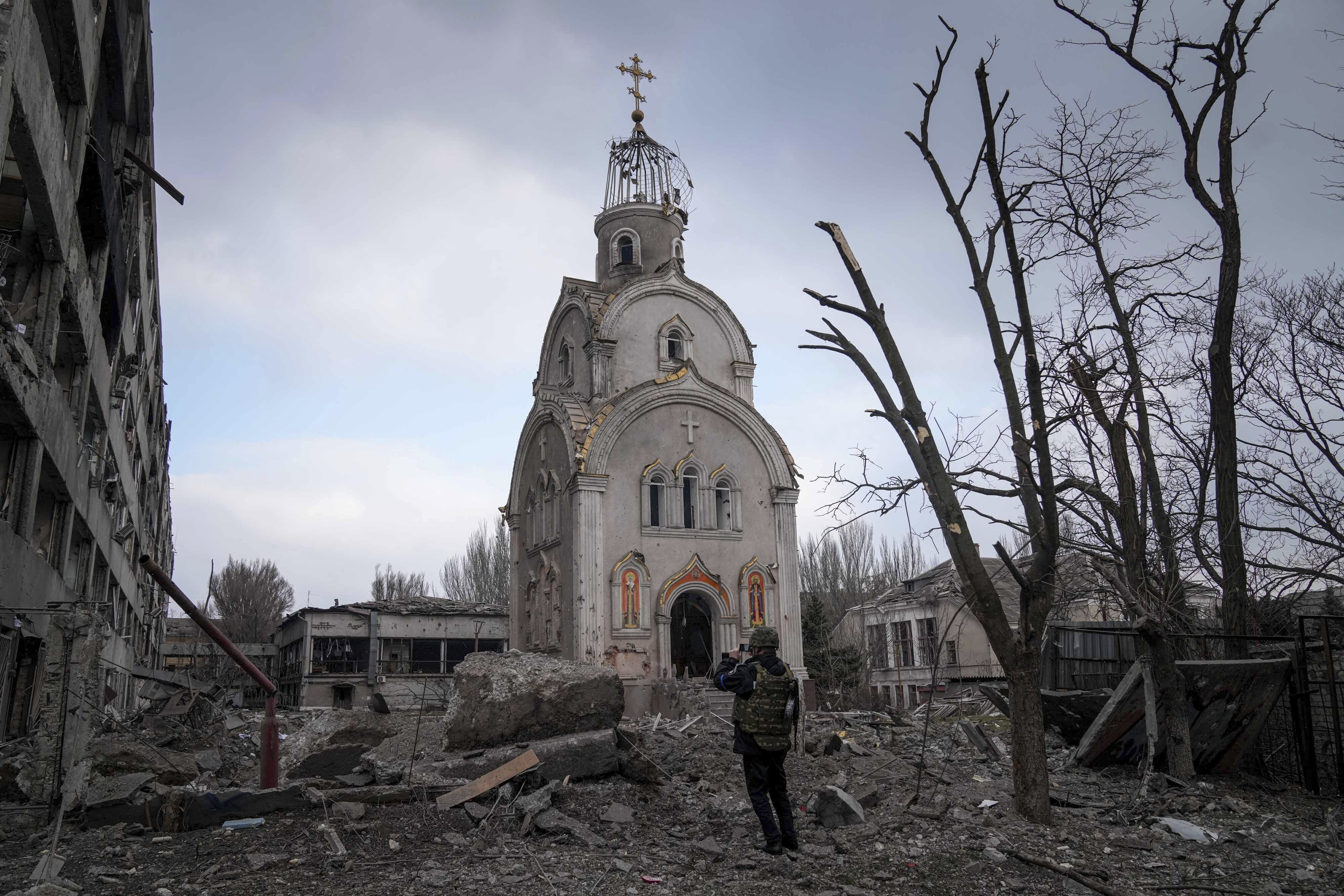 A Ukrainian serviceman takes a photograph of a damaged church