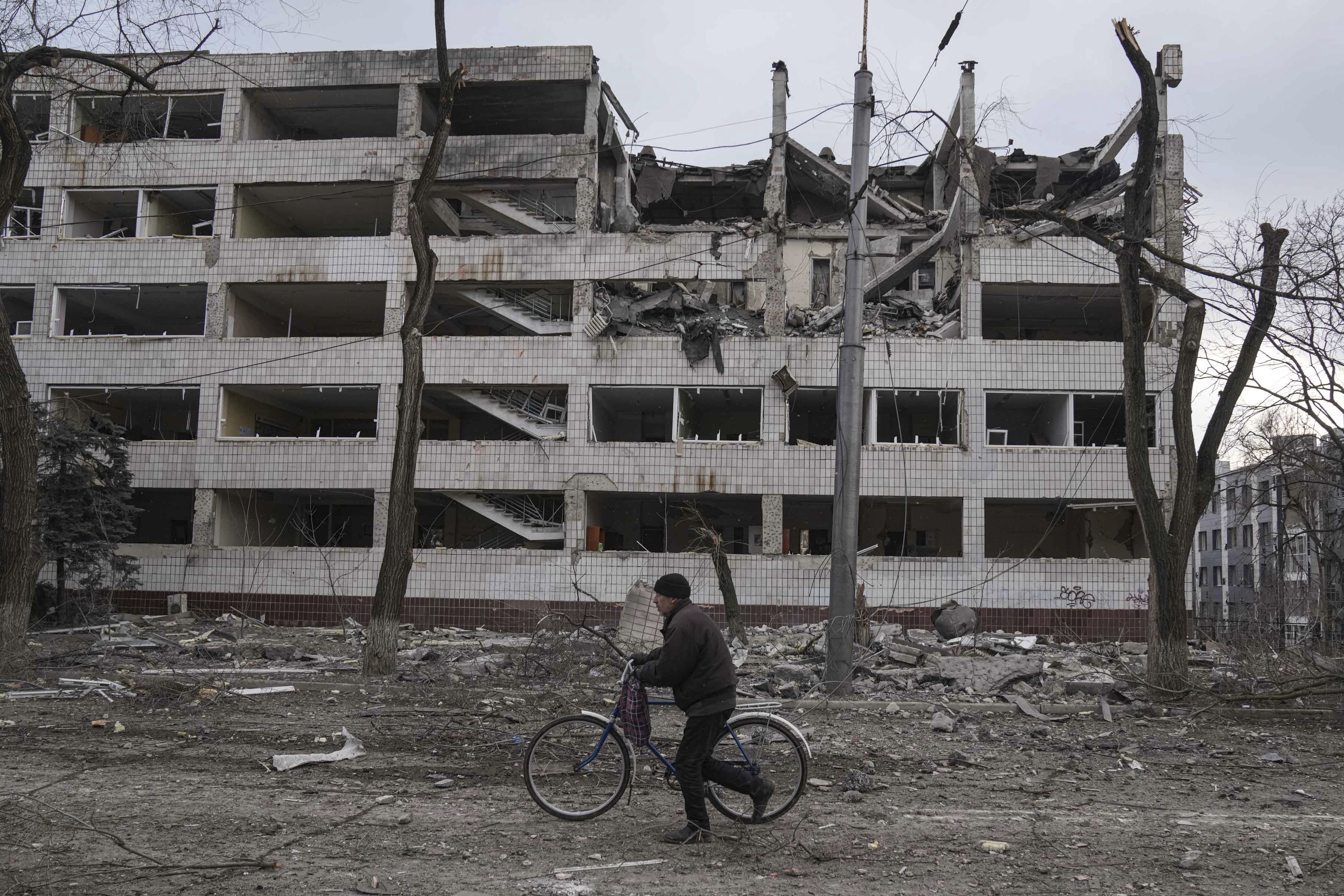 A man walks with a bicycle in front of a damaged by shelling in Mariupol, Ukraine