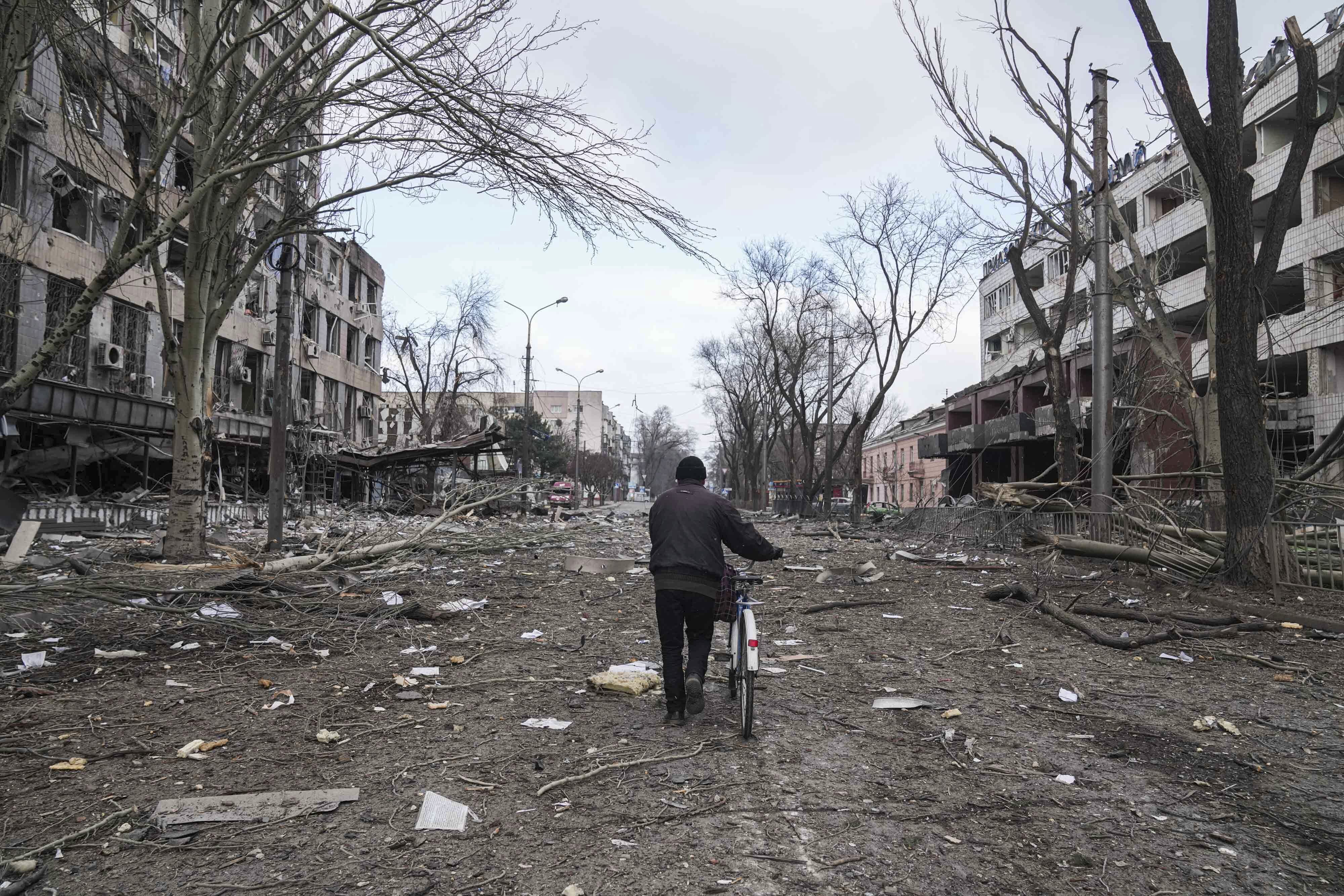 A man walks with a bicycle in a street damaged by shelling in Mariupol, Ukraine, Thursday
