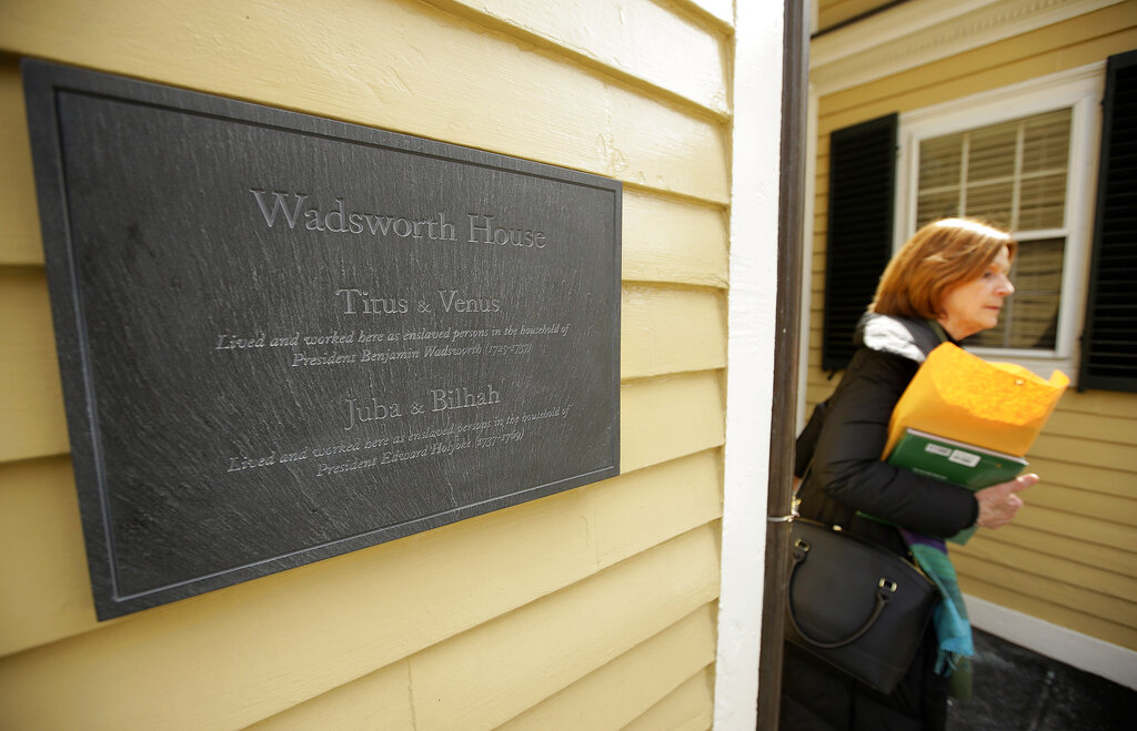 A passer-by walks near a plaque attached to Wadsworth House on the campus of Harvard University, that honors four slaves that had been owned by and worked for Harvard's past presidents, in Cambridge, Mass.