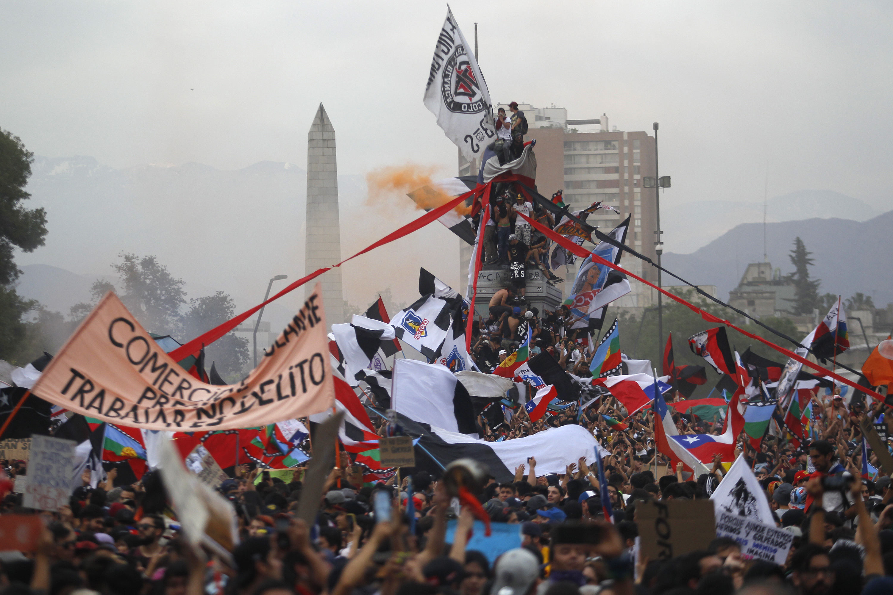 Protesters wave Chilean flags and climb the monument to General Baquedano
