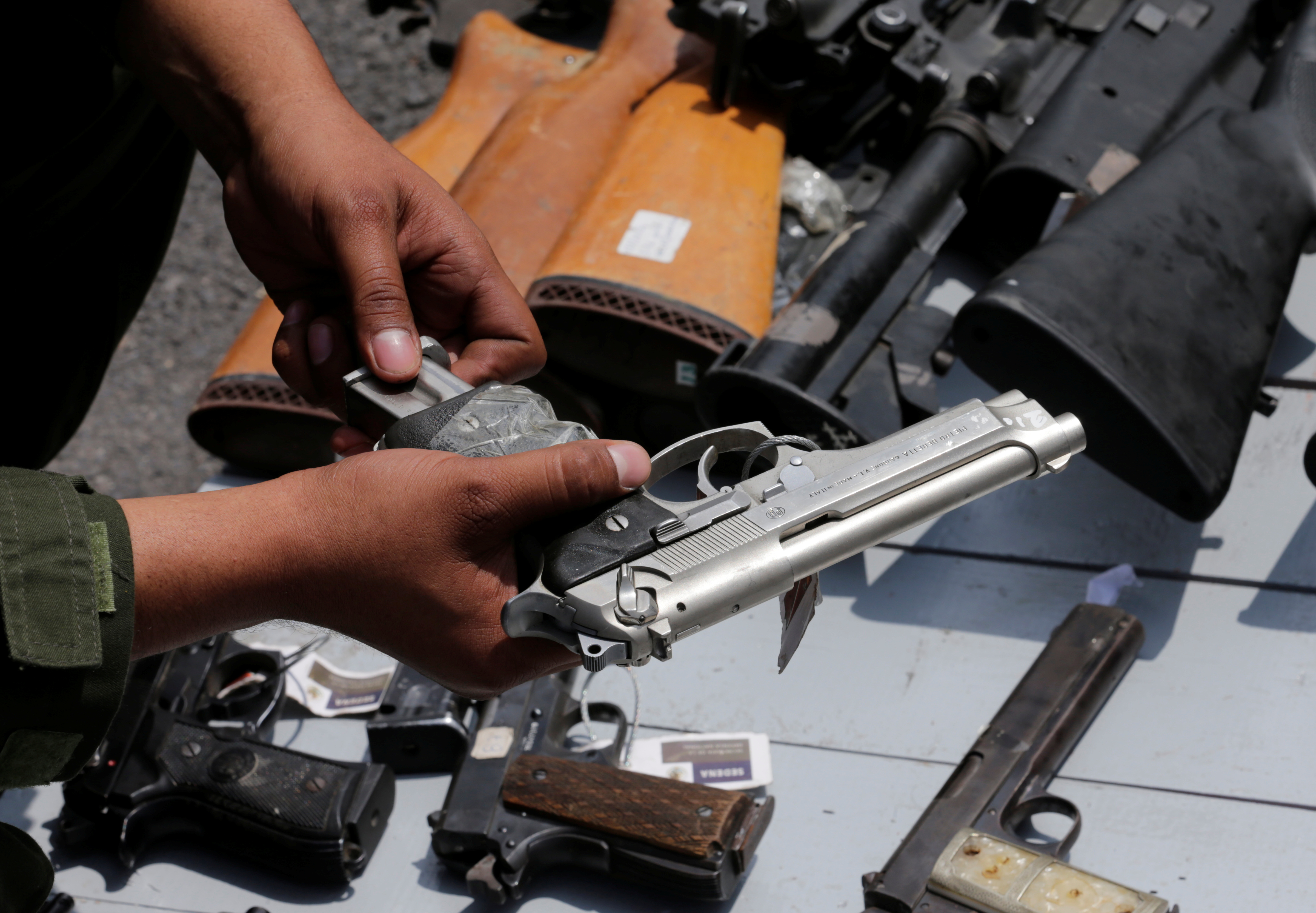 A Mexican soldier holds up a gun next to other weapons seized from alleged drug traffickers or handed in by residents.