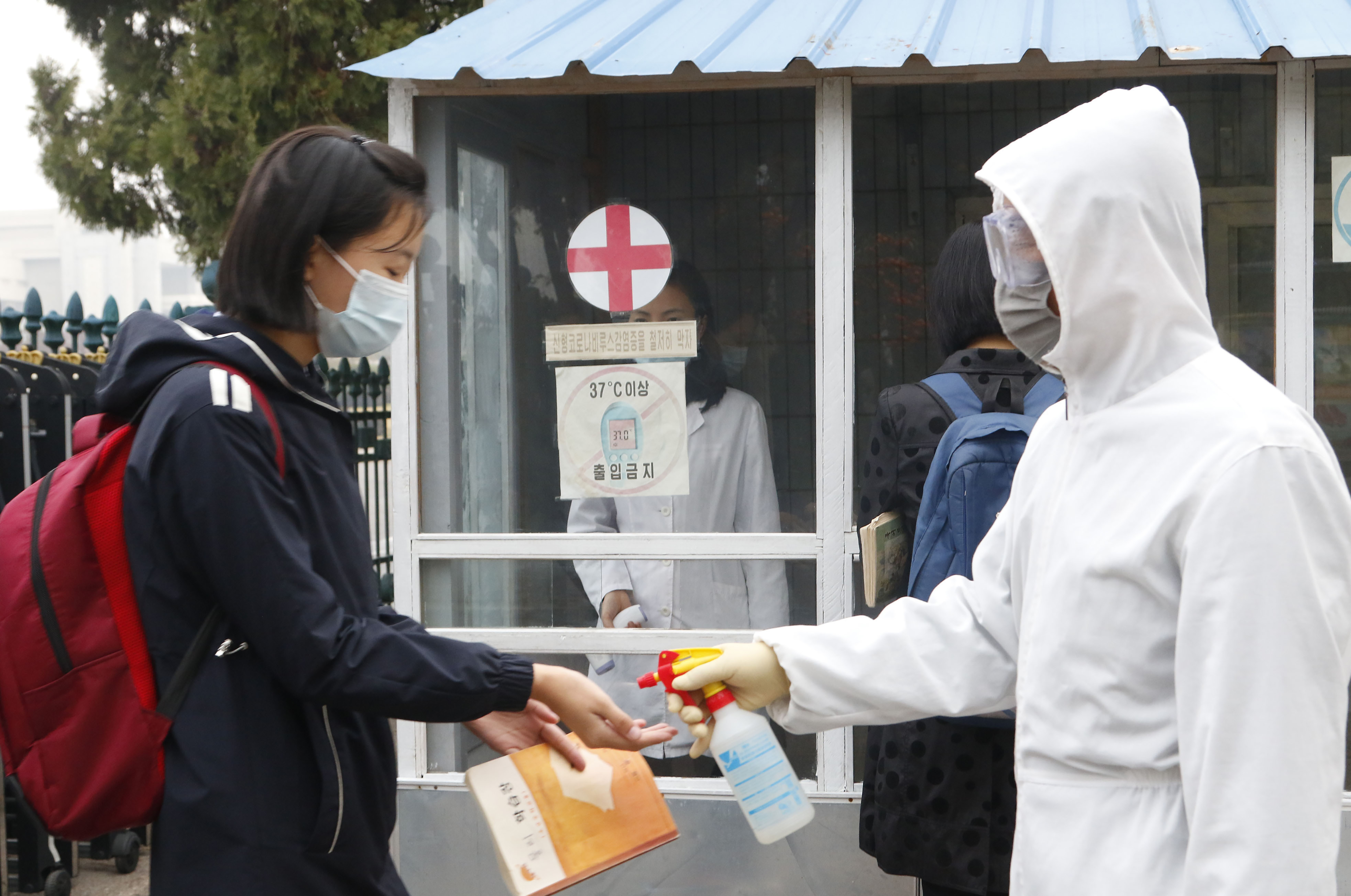 A schoolgirl in a face mask has her hands disinfected by a worker in a hazmat suit at the entrance to a Pyongyang secondary school