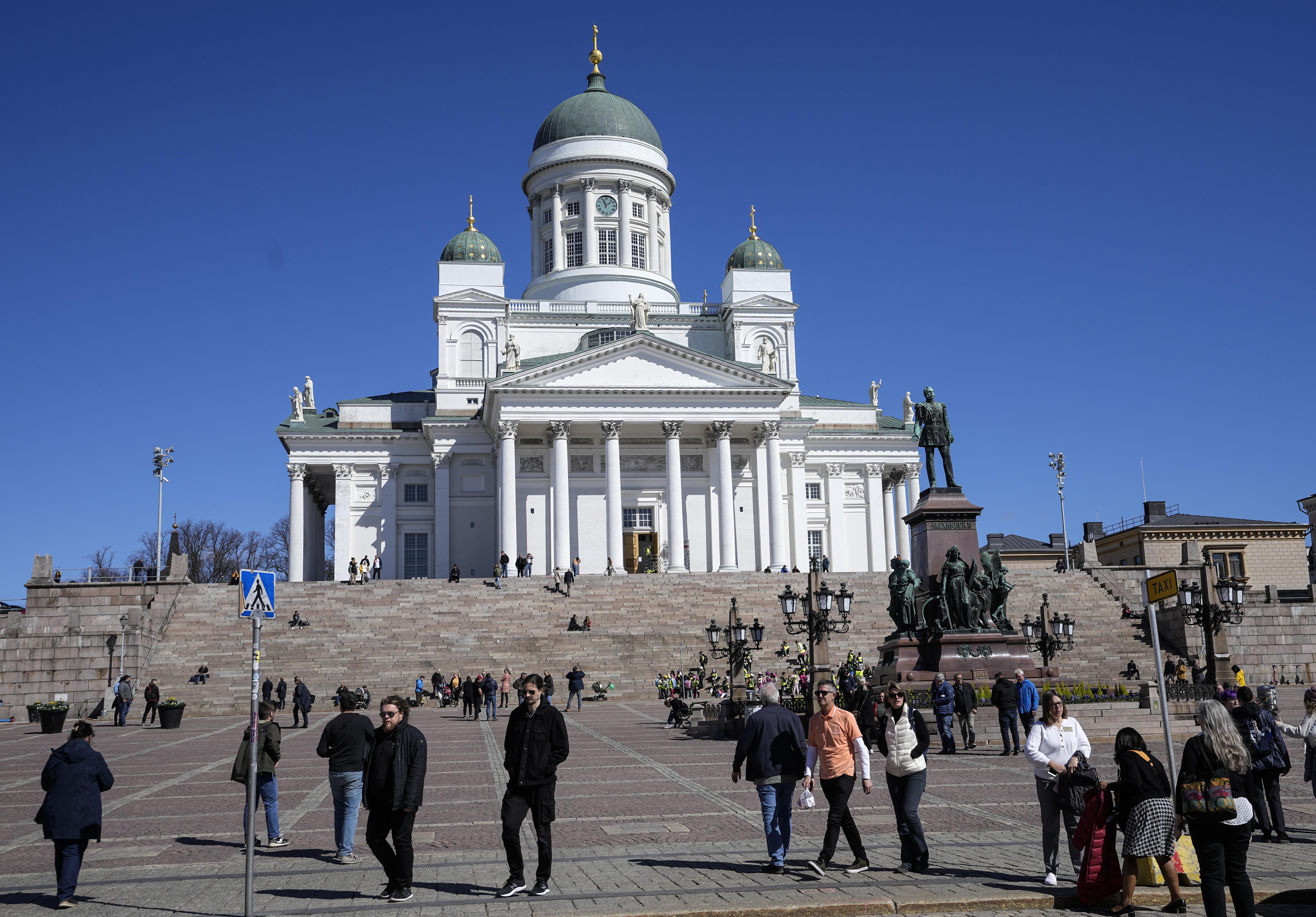 People walk at the Helsinki Cathedral under a blue sky in the city center of Helsinki, Finland, Friday, May 13, 2022.