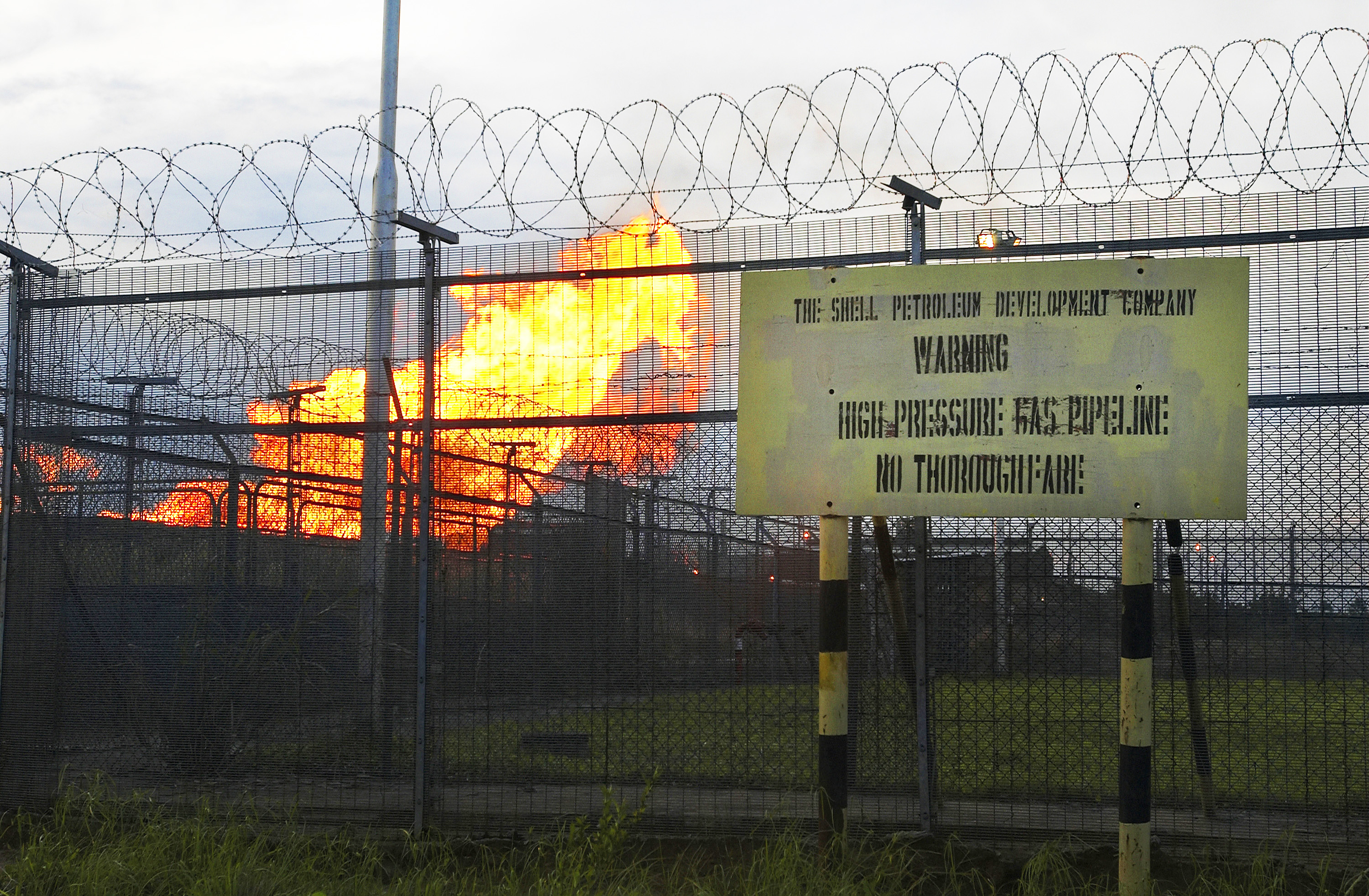 Associated natural gas burns at a flaring site behind a security fence