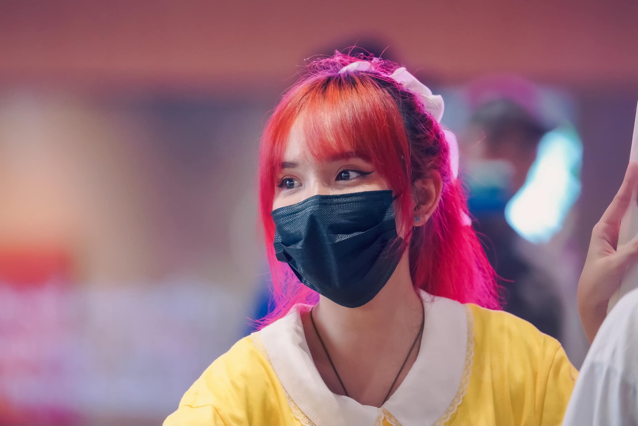 A portrait of Maynu with pink hair and wearing a black face mask 