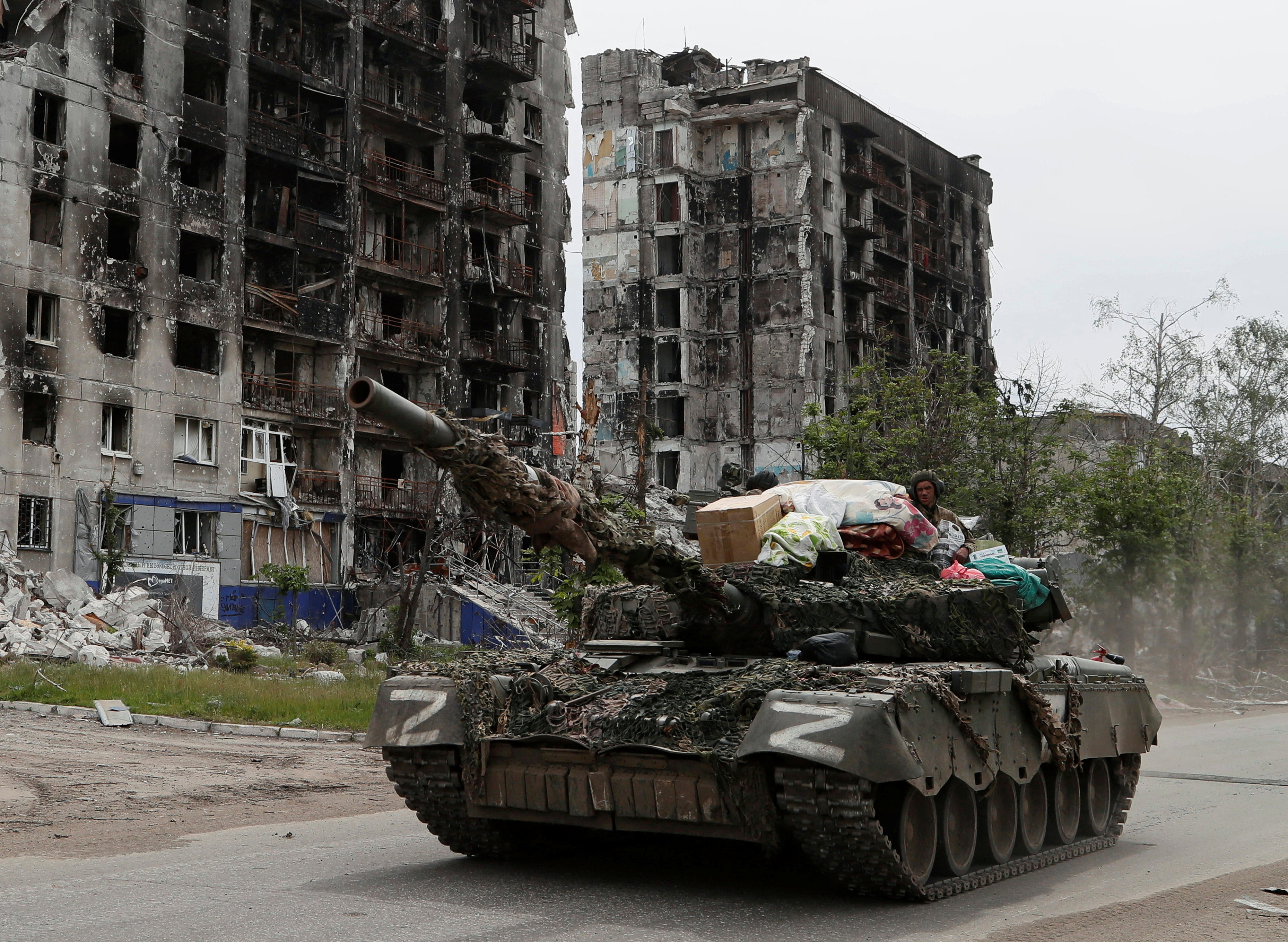 Service members of pro-Russian troops drive a tank past destroyed residential buildings in the town of Popasna in the Luhansk Region