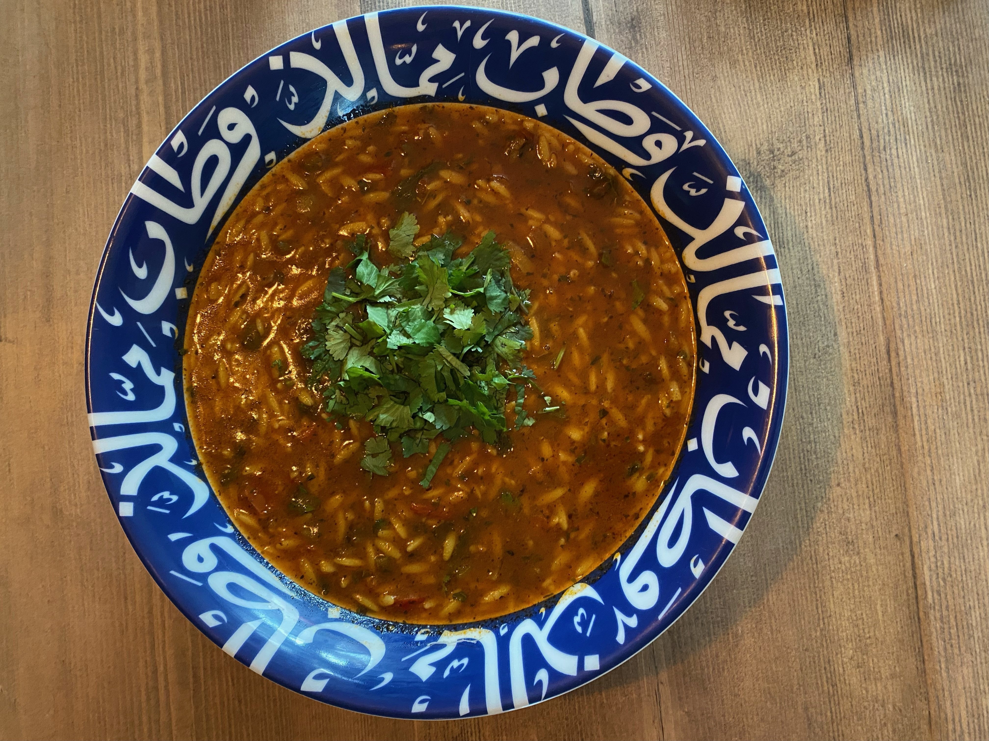 A bowl of sherba soup sits on a wooden table top