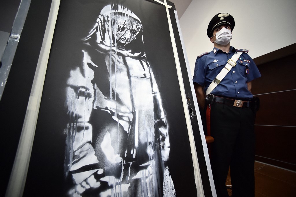 a policeman stands guard near a piece of art attributed to Banksy, that was stolen at the Bataclan in Paris in 2019, and found in Italy,