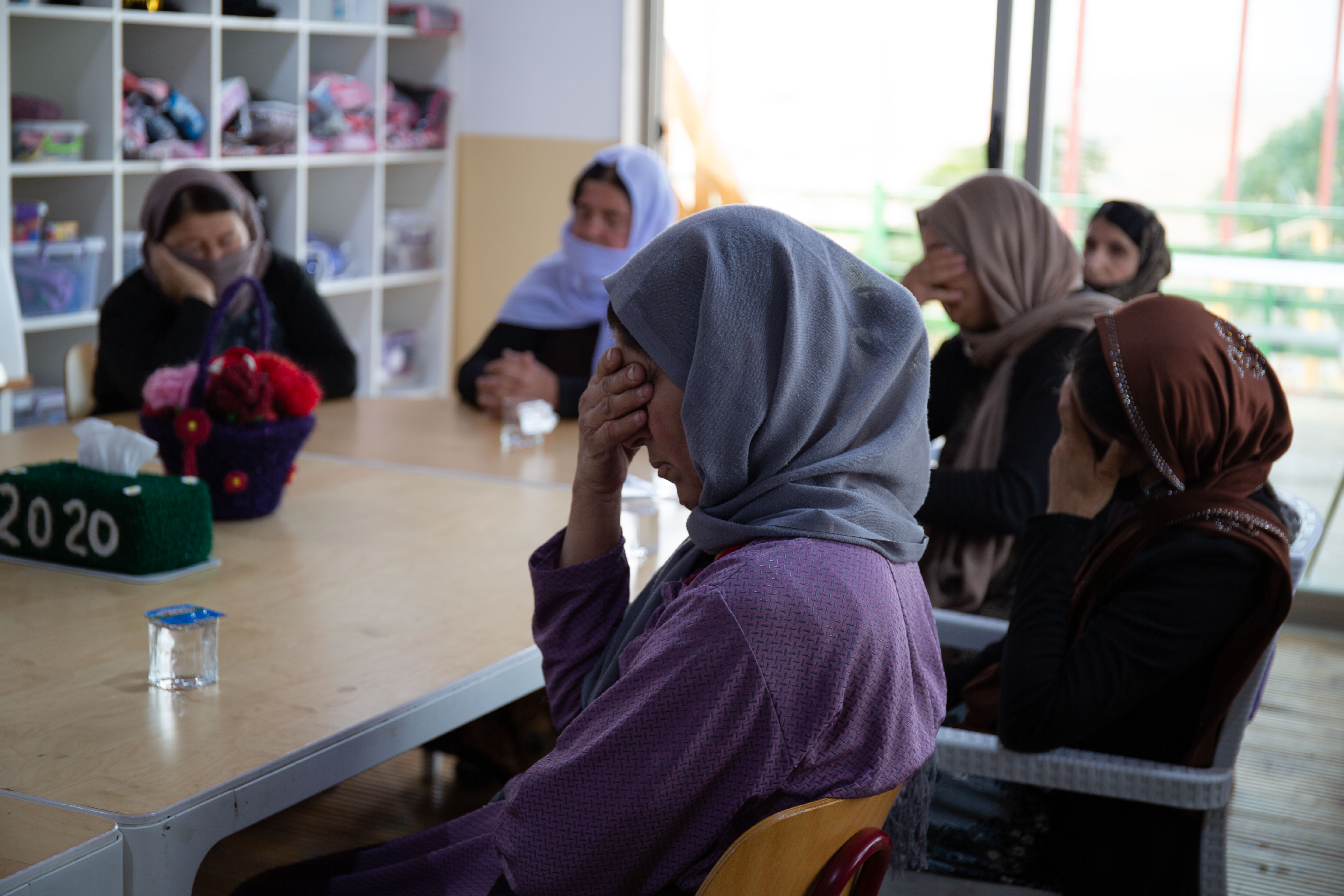 A photo of a group of women sitting around a table with their eyes closed.