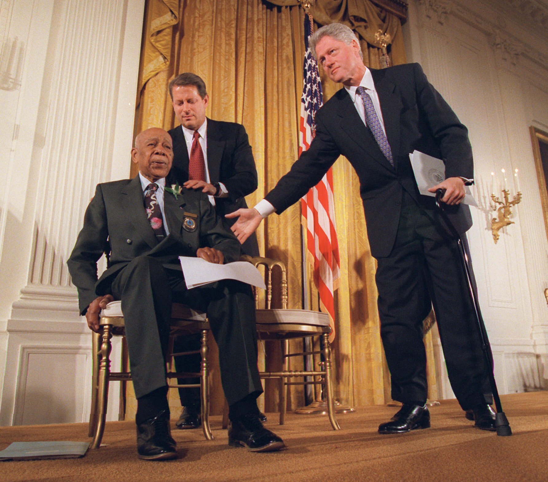 US President Bill Clinton and Vice President Al Gore, back, help Herman Shaw, 94, a Tuskegee Syphilis Study victim, during a news conference in 1997 [File photo: Doug Mills/AP]