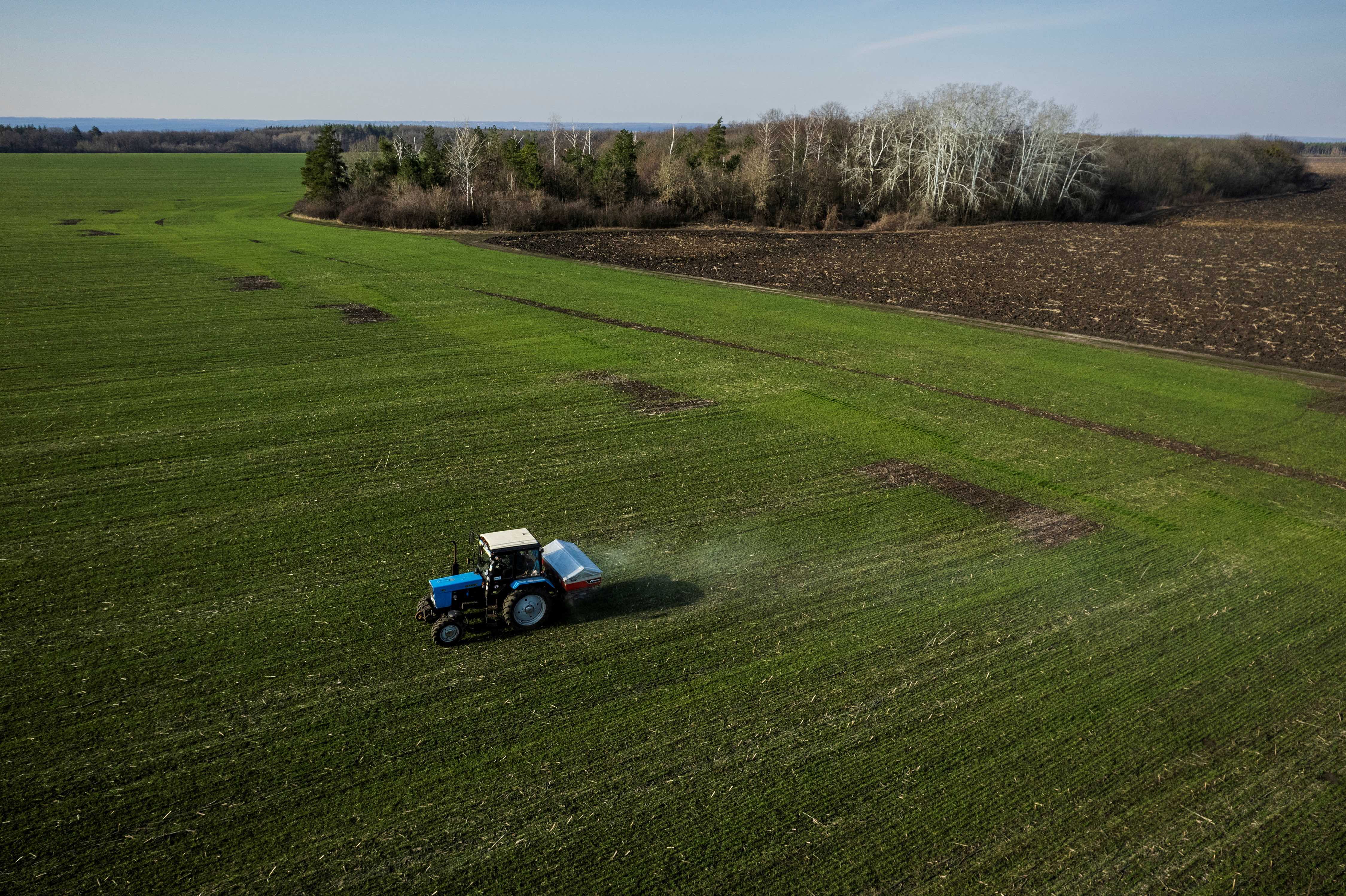 An aerial view shows a tractor spreading fertiliser on a wheat field near the village of Yakovlivka after it was hit by an aerial bombardment outside Kharkiv, as Russia's attack on Ukraine continues