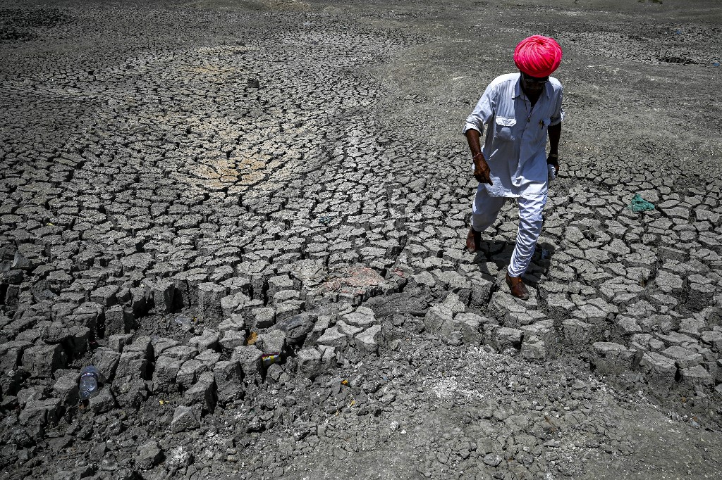 villager walking through the cracked bottom of a dried-out pond on a hot summer day at Bandai village in Pali distric