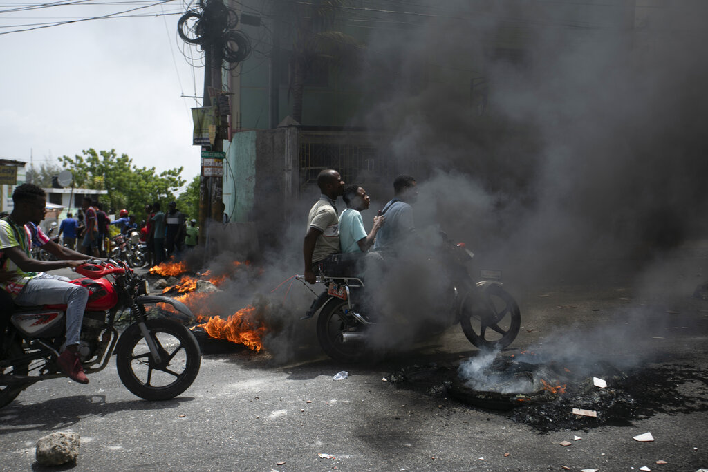 A motorcycle taxi driver carries clients past a burning barricade