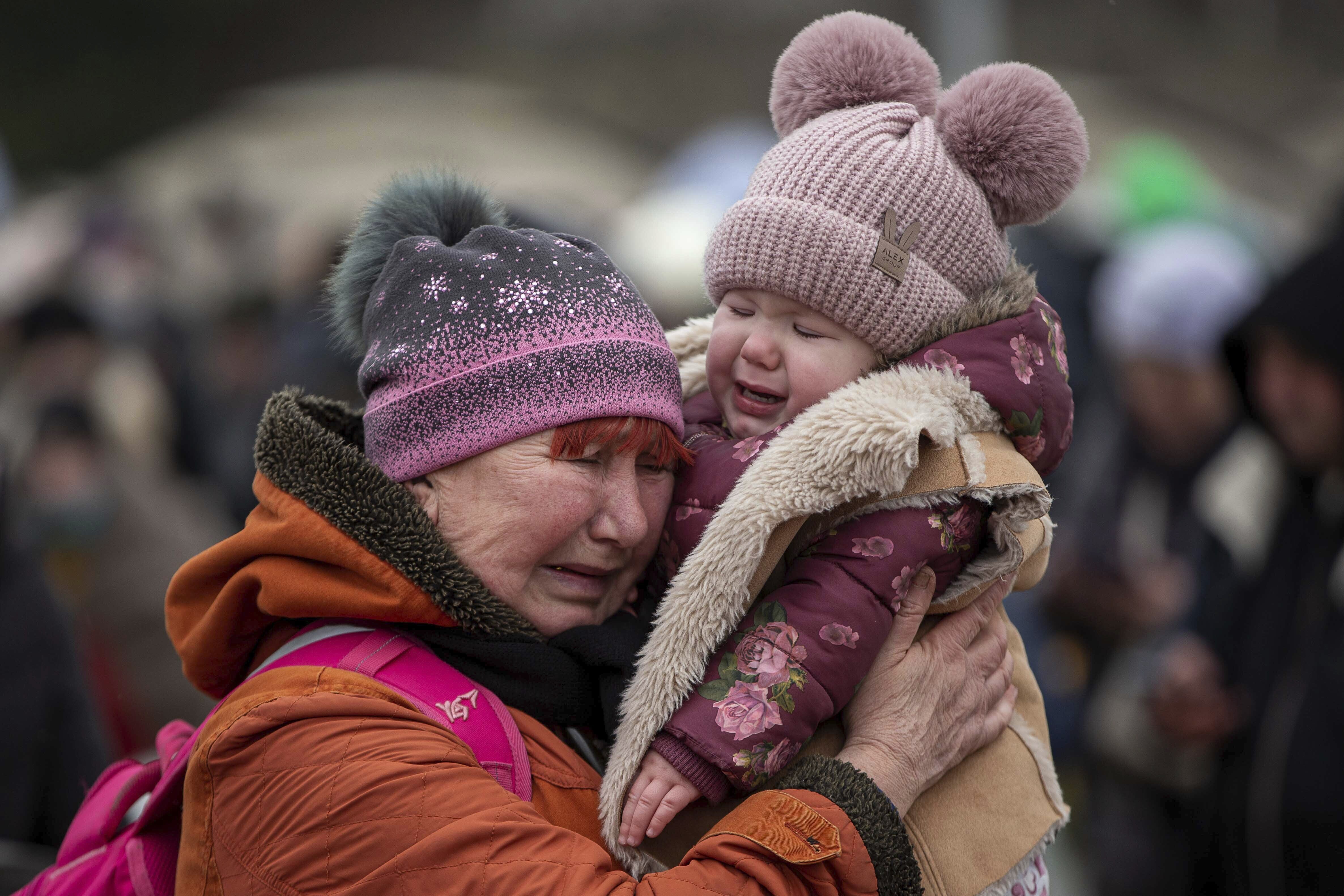 A woman holding a child cries after fleeing from the Ukraine and arriving at the border crossing in Medyka, Poland