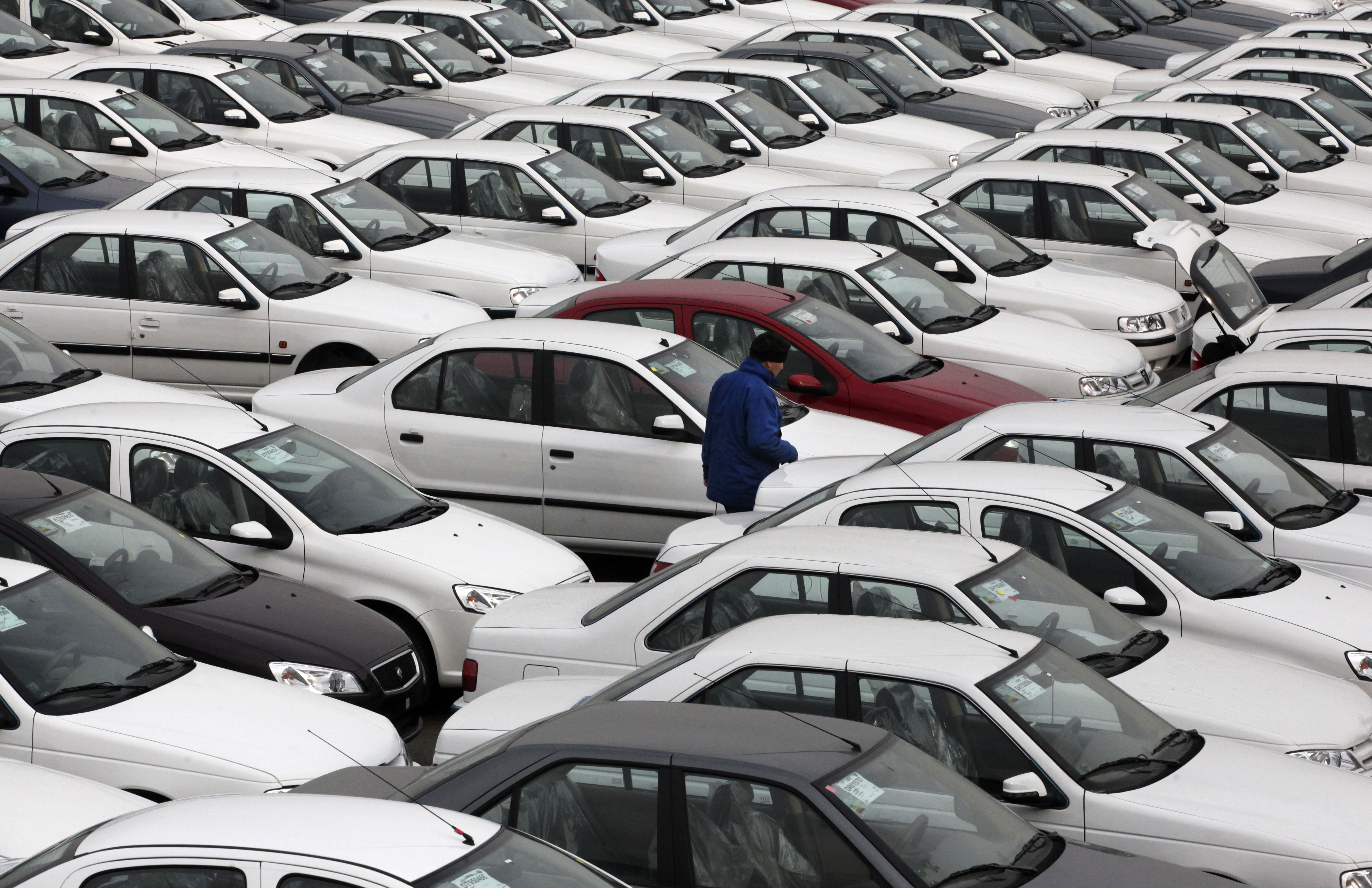 An Iranian worker walks among cars in a depot at the Iran Khodro automobile manufacturing plant, just outside Tehran, Iran