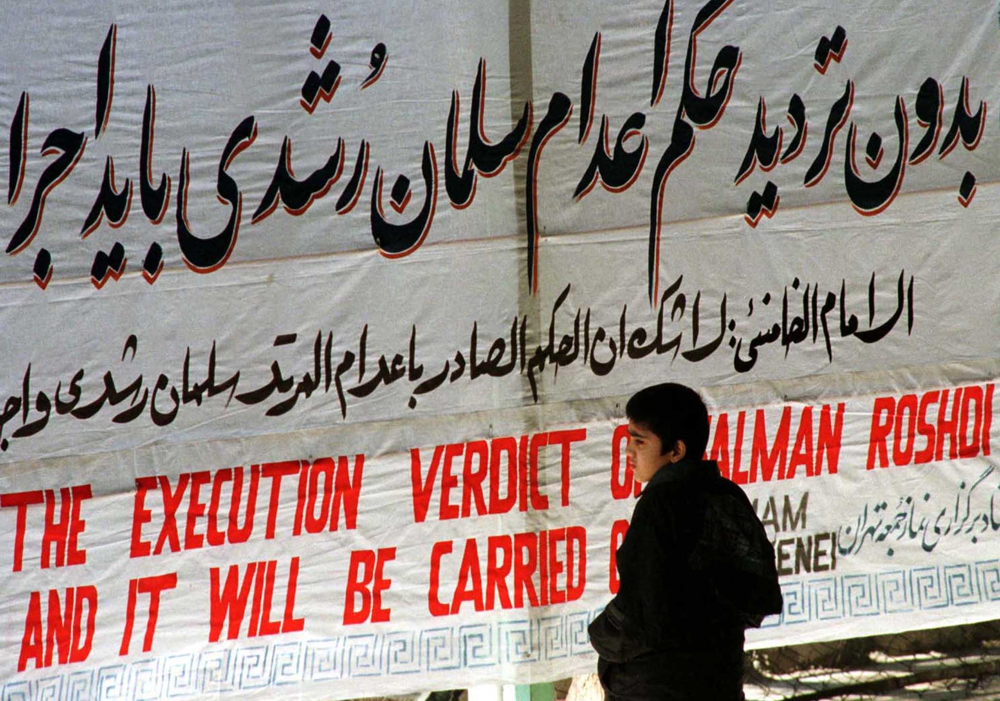 An Iranian boy stands in front of a banner at Tehran University in 1989 that reads ‘the execution verdict of Salman Rushdie will be carried out’