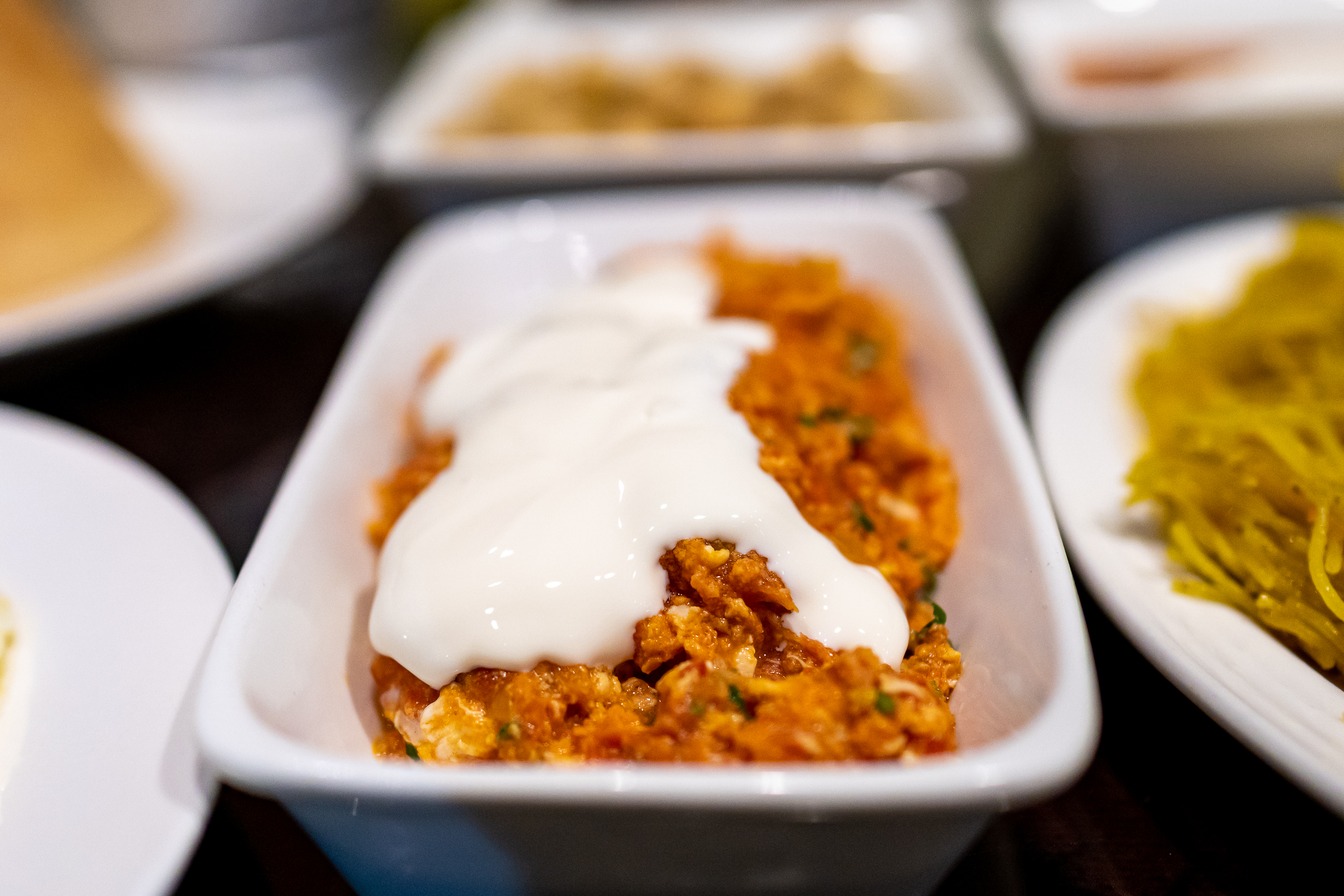 A rectangular dish of tomatoey scrambled eggs with a dollop of white processed cheese spread on top