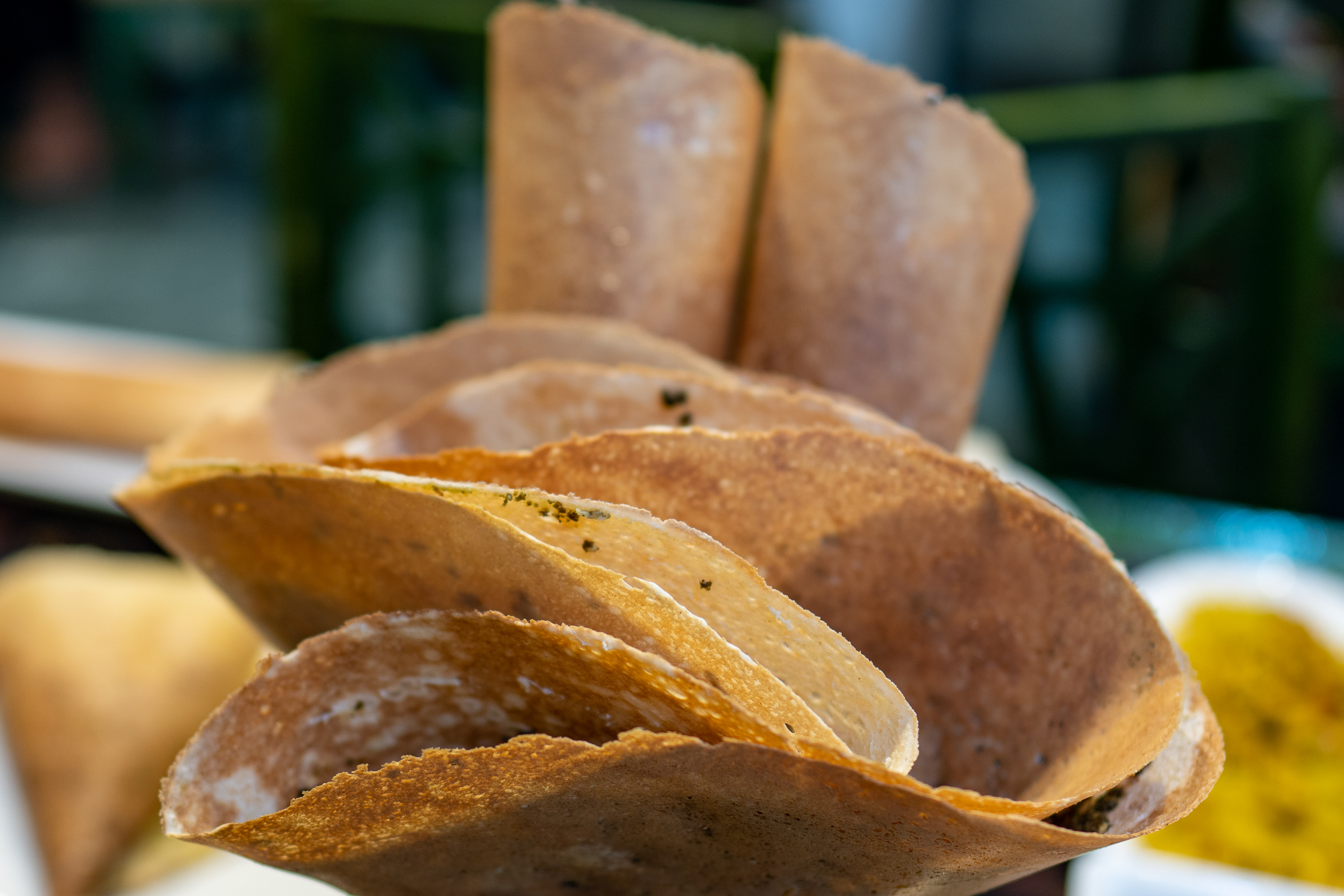A closeup shot of a bucket of regag bread, the folded ones in the foreground have a sprinkling of zaatar inside them while the rolls of regag in the back are sweet, with sugar sprinkled inside