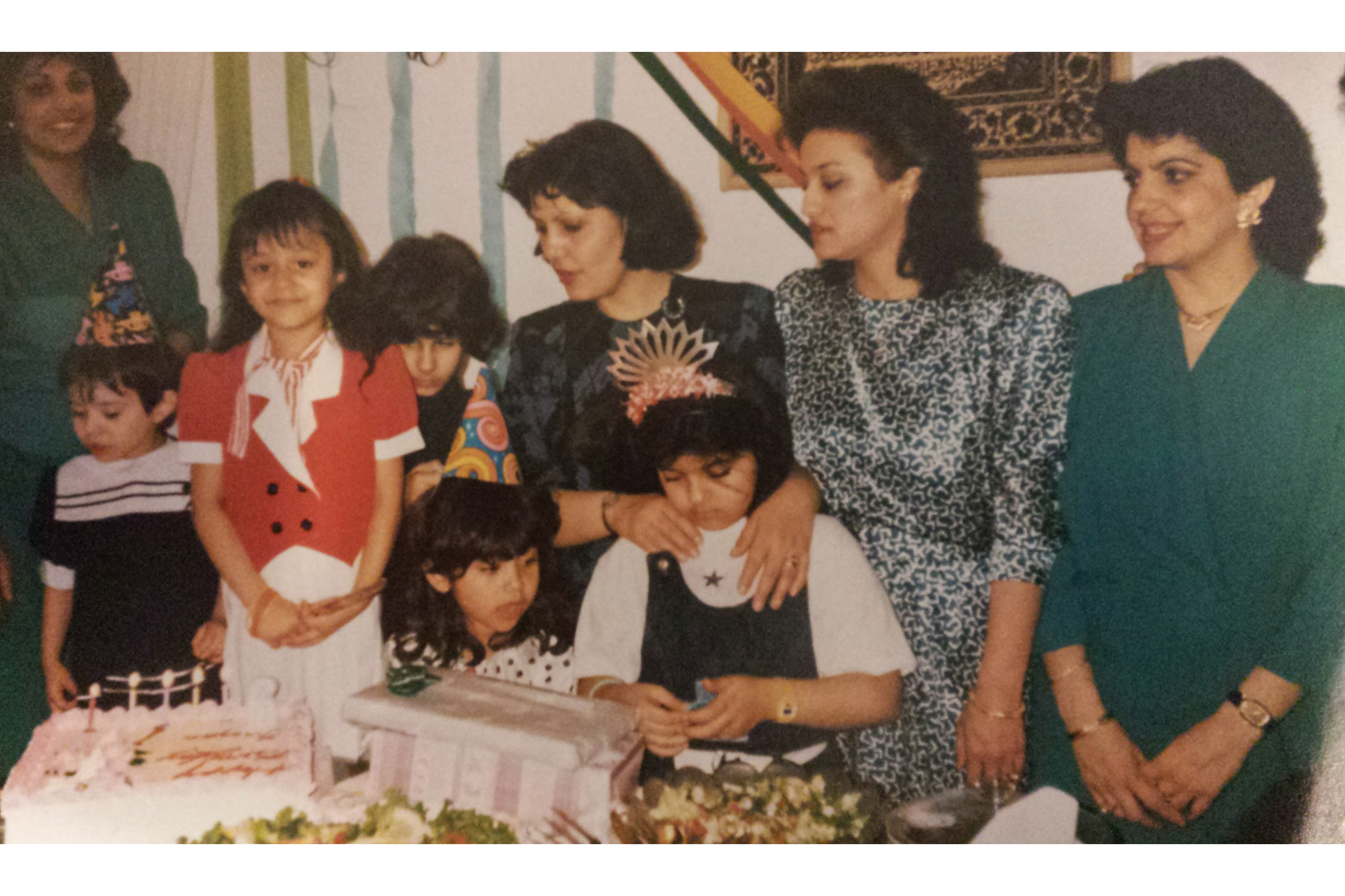 Mina with her mother standing behind her with her hands on her shoulders, along with her aunts and cousins over a birthday feast featuring kebab [Courtesy of Mina Sharif]