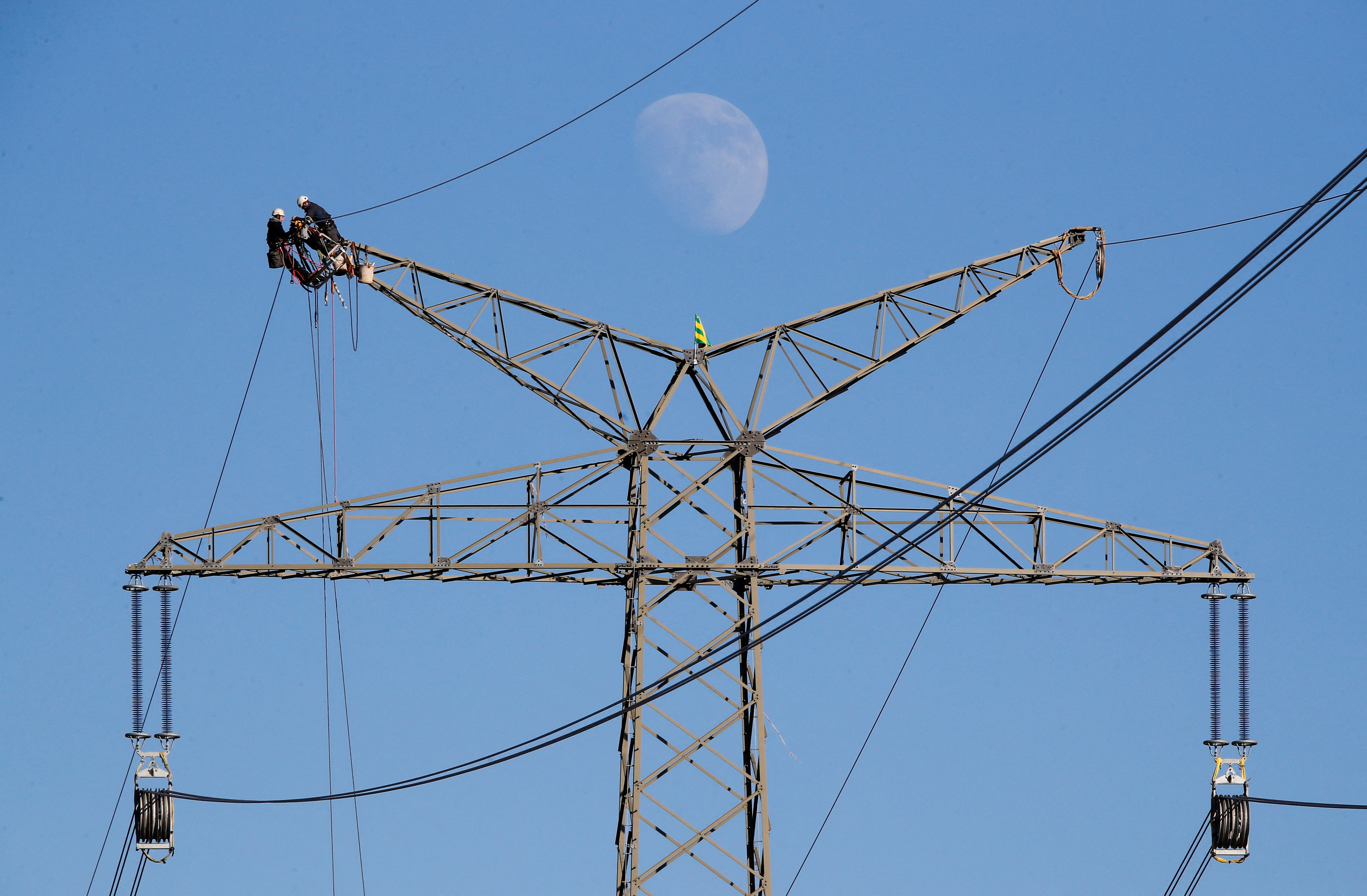 The moon rises as electricians work atop a power pole near the lignite power plant of Neurath of German energy supplier and utility RWE, near Rommerskirchen north-west of Cologne, Germany, February 5, 2020.