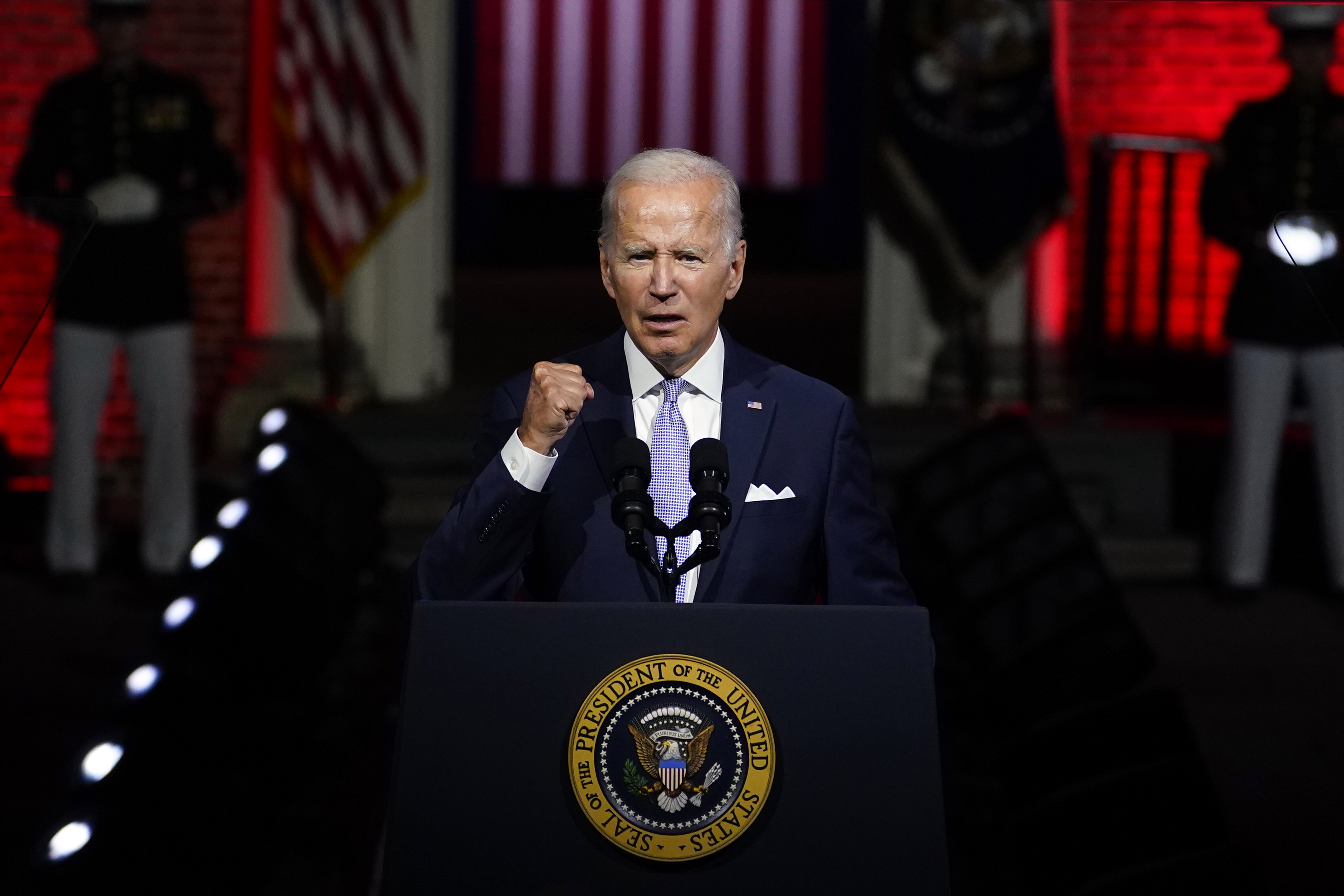 US President Joe Biden, speaking from behind a lectern, clenches his fist as he makes a point