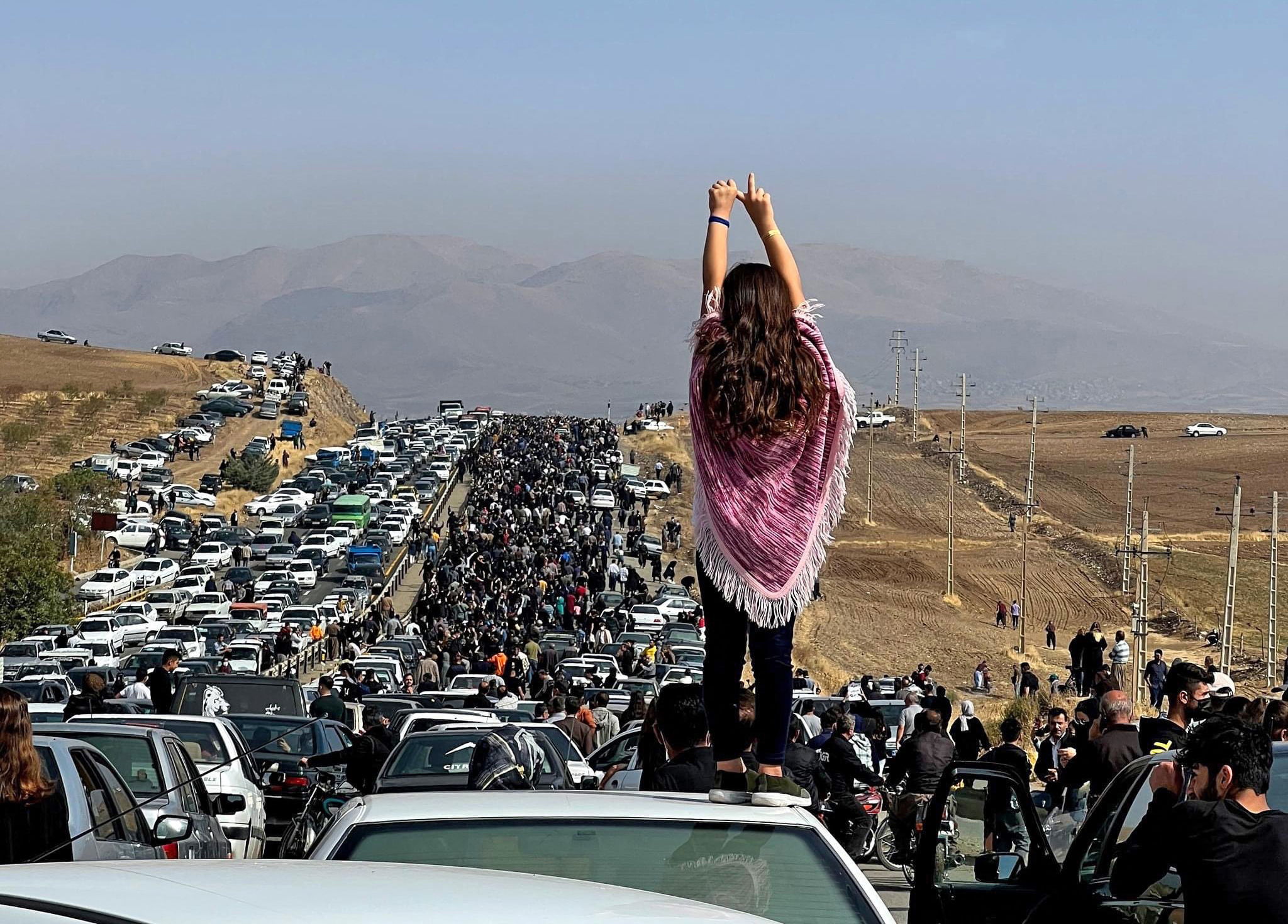 This image posted on Twitter shows an unveiled woman standing on top of a vehicle as thousands make their way towards Aichi cemetery in Saqqez, Mahsa Amini’s hometown in the western Iranian province of Kurdistan, to mark 40 days since her death, defying heightened security measures as part of a bloody crackdown on women-led protests [AFP]