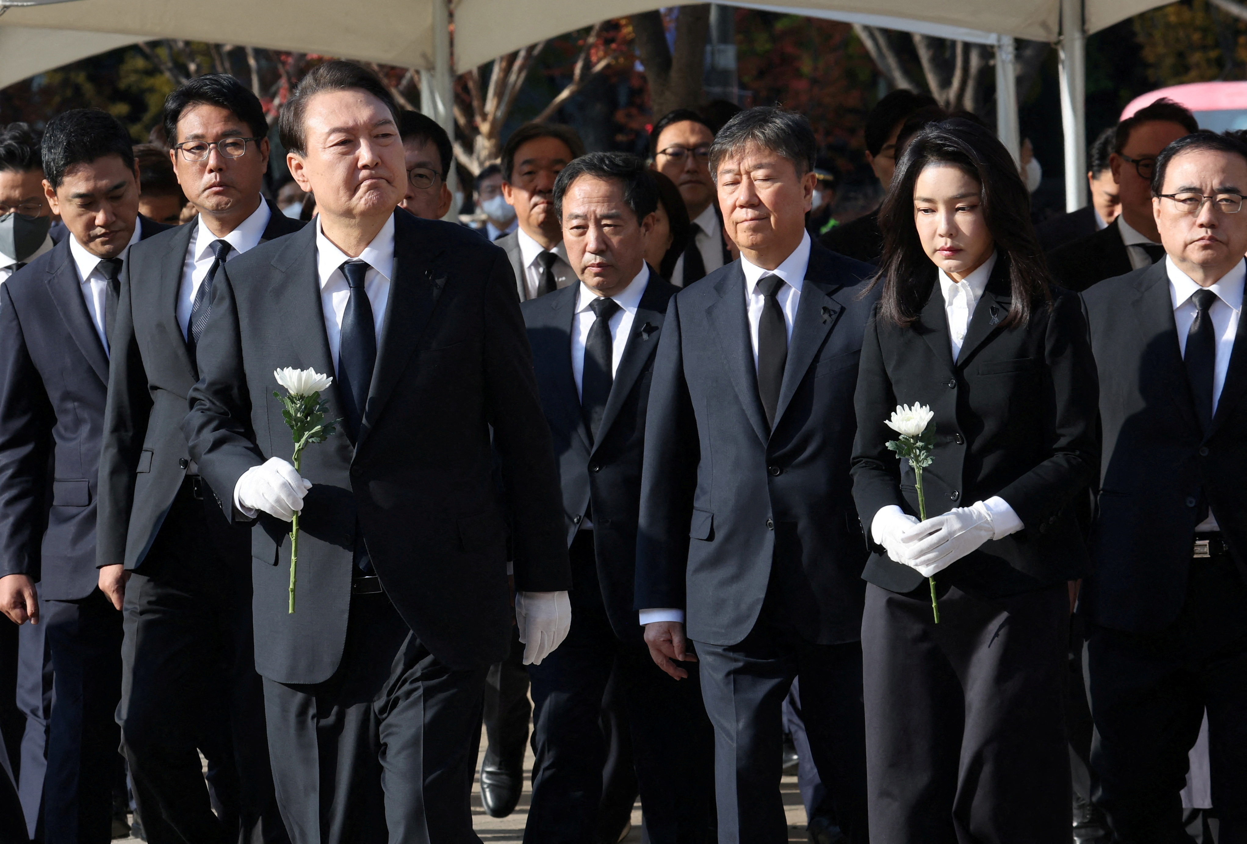 In black suits with white gloves, South Korean President Yoon Suk-yeol and his wife Kim Keon-hee hold white flowers as they visit a memorial altar for victims of the Itaewon crush in Seoul, South Korea.