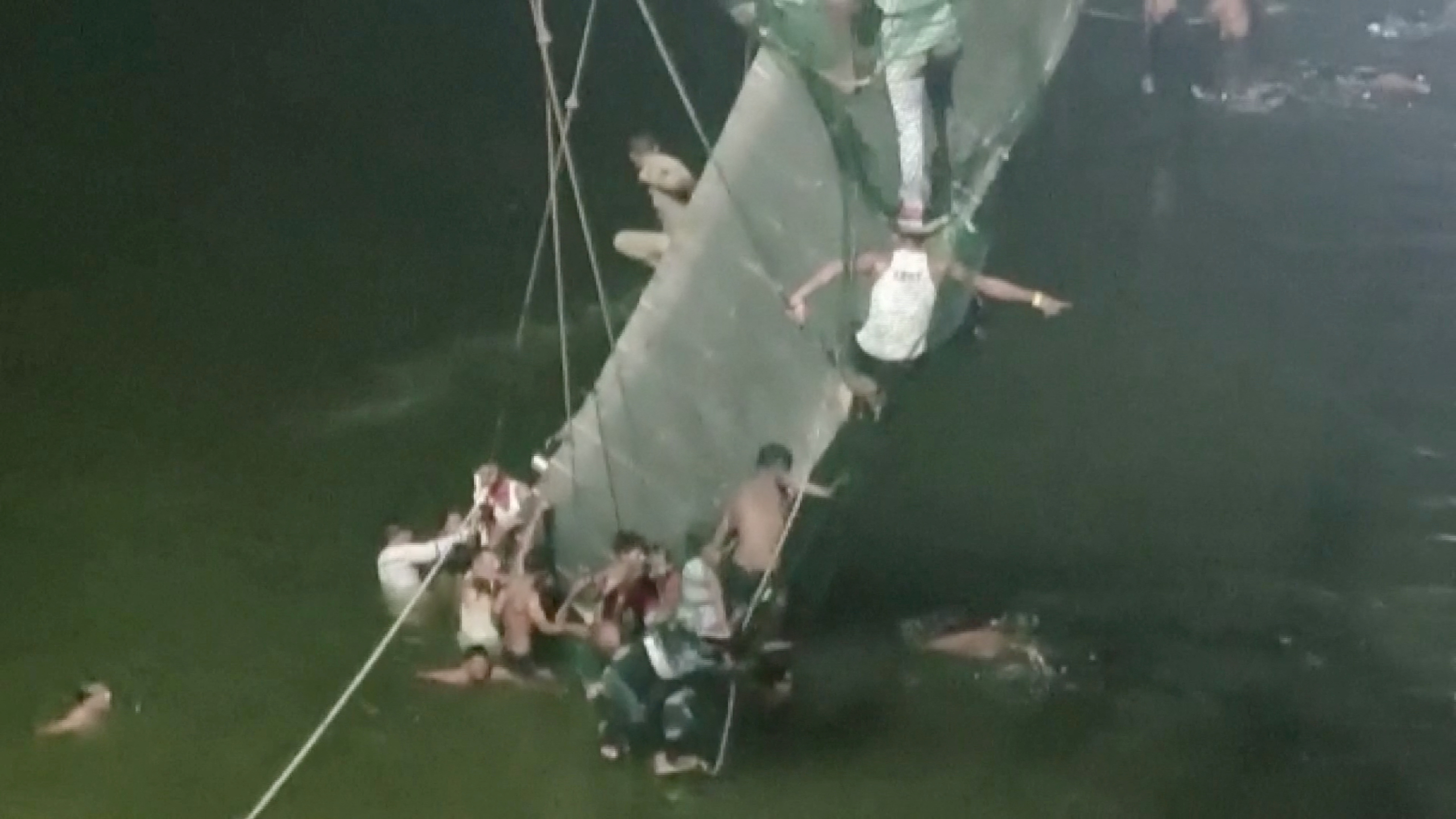 People cling to the collapsed suspension bridge in Morbi