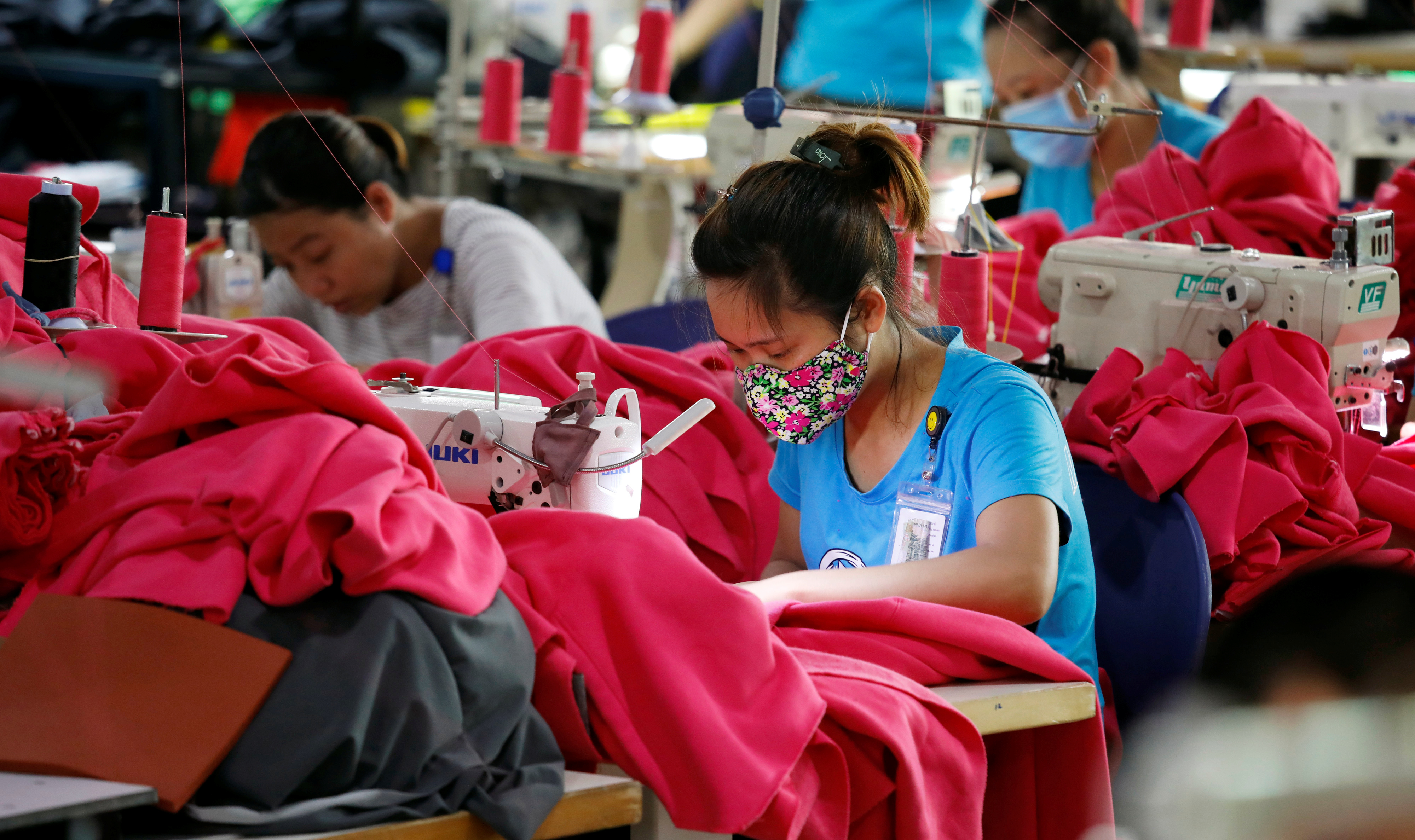 Asian women in factory at sewing machines working on red garments
