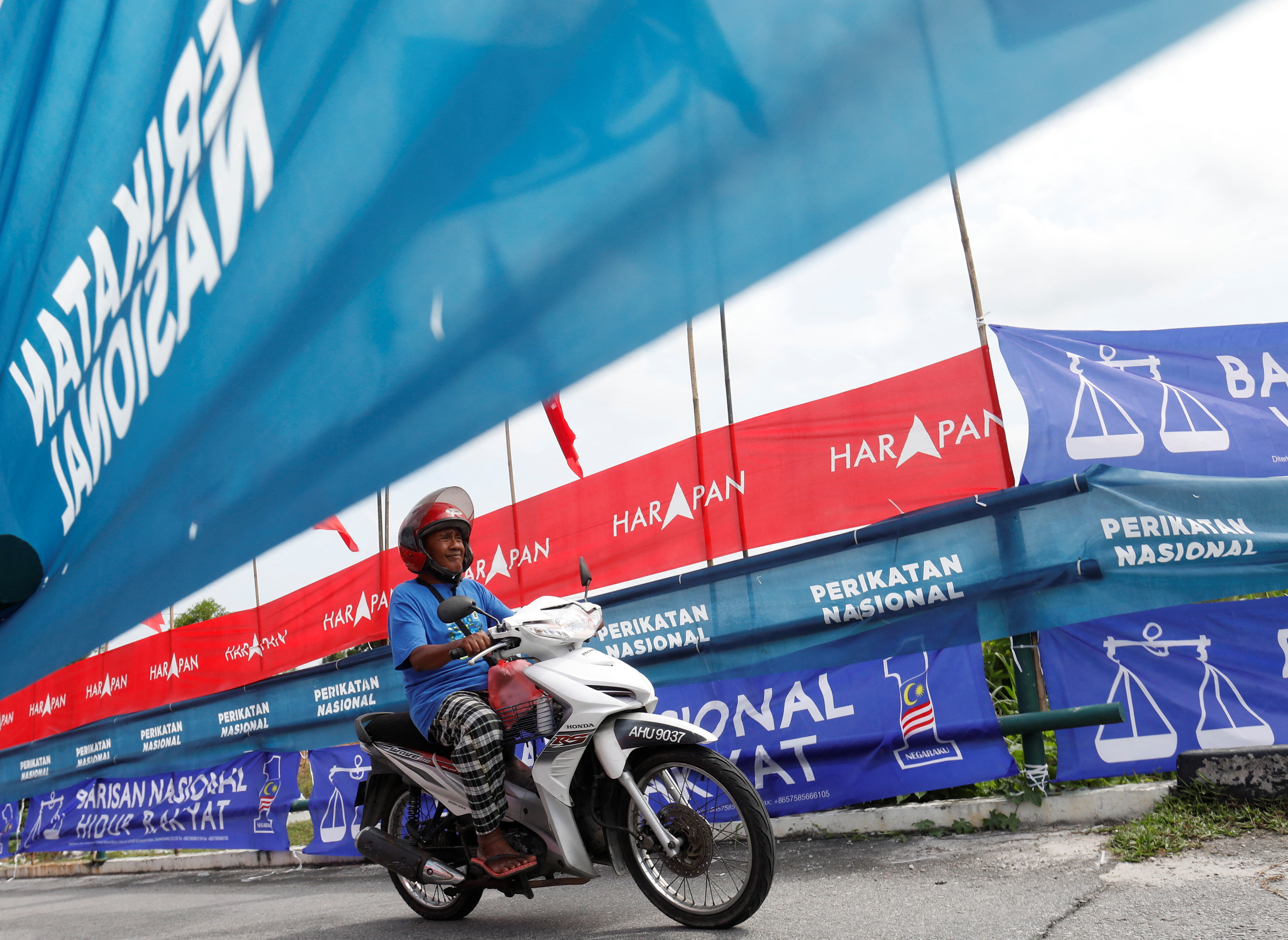 A man on a motorbike drives alongside flags over Malaysia's three main coalition groupings during the 2022 election campaign