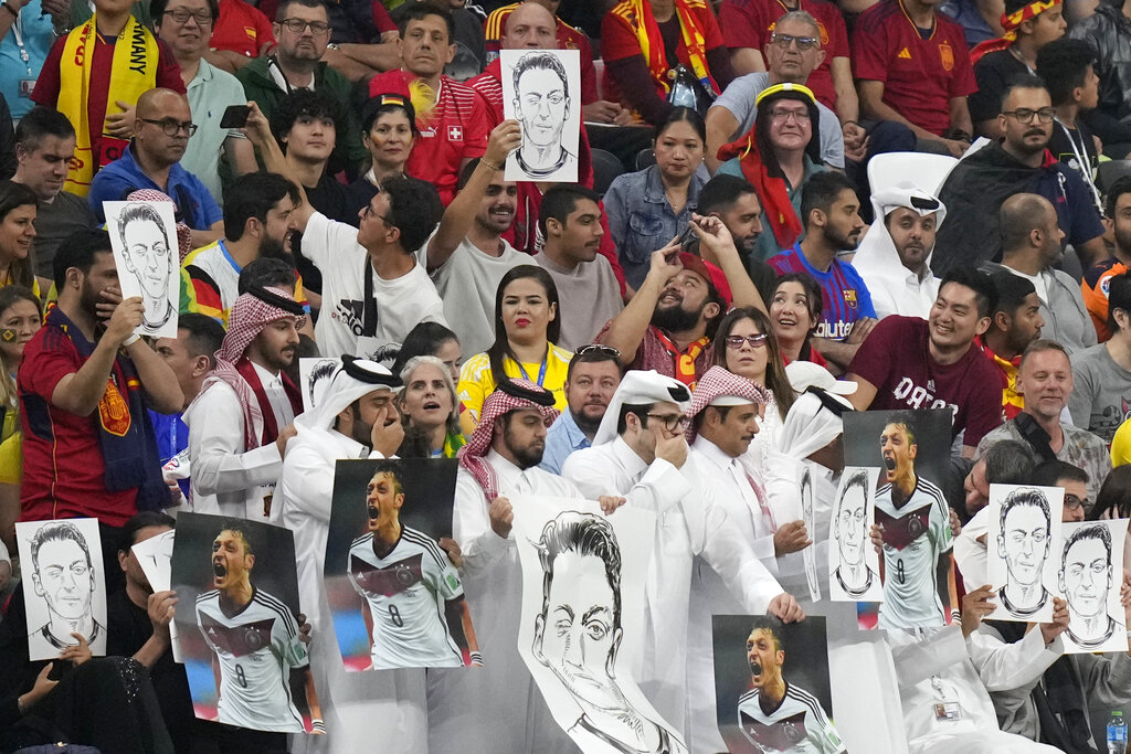 Spectators hold photos of former German international player Mesut Ozil on the stands and cover their mouths during the World Cup Group E football match between Spain and Germany, at the Al Bayt Stadium in Al Khor, Qatar, on November 27, 2022