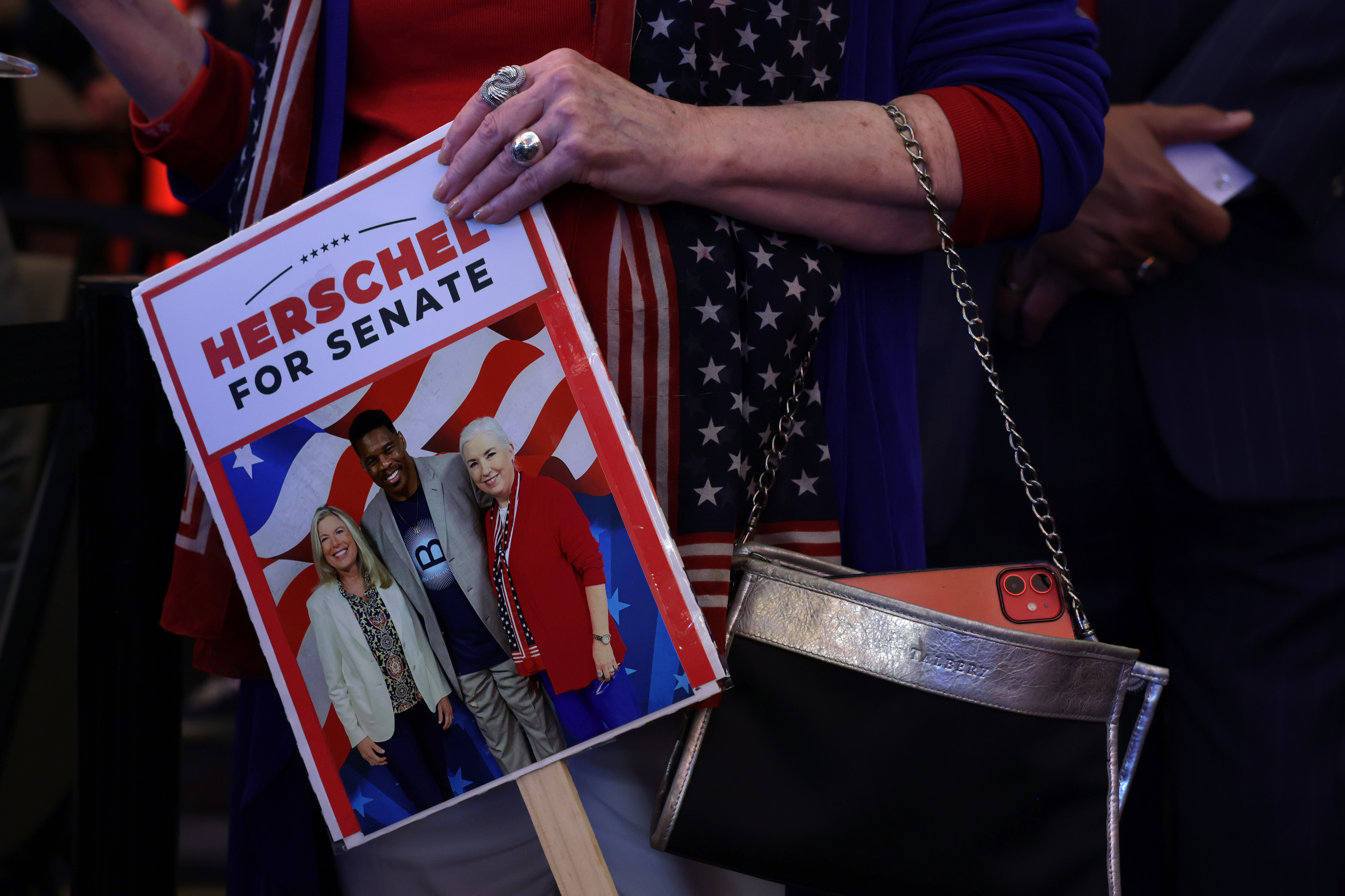 A hand holds a sign that reads, 'Herschel for Senate'