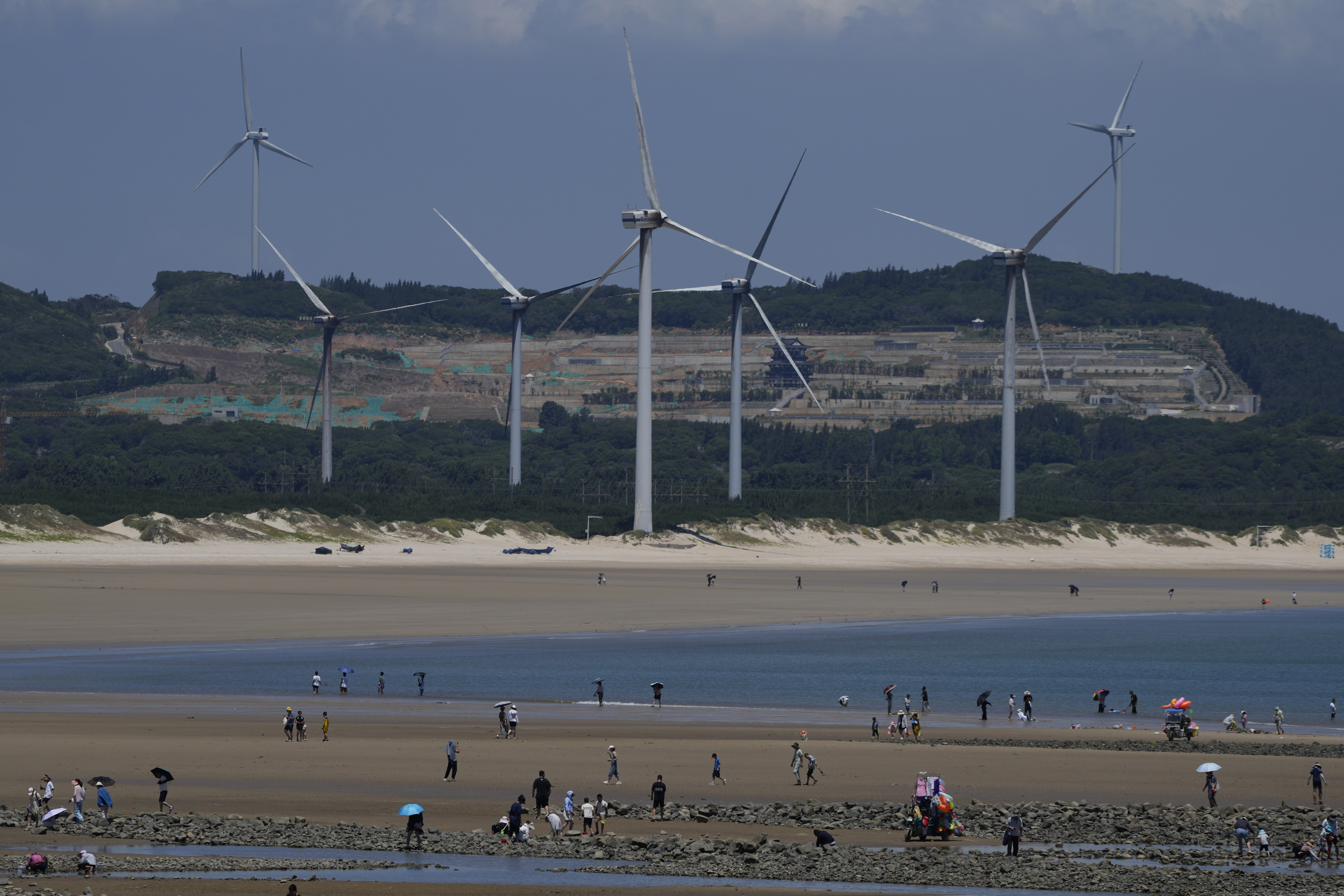Beachgoers walk near wind turbines along the coast of Pingtan in Southern China