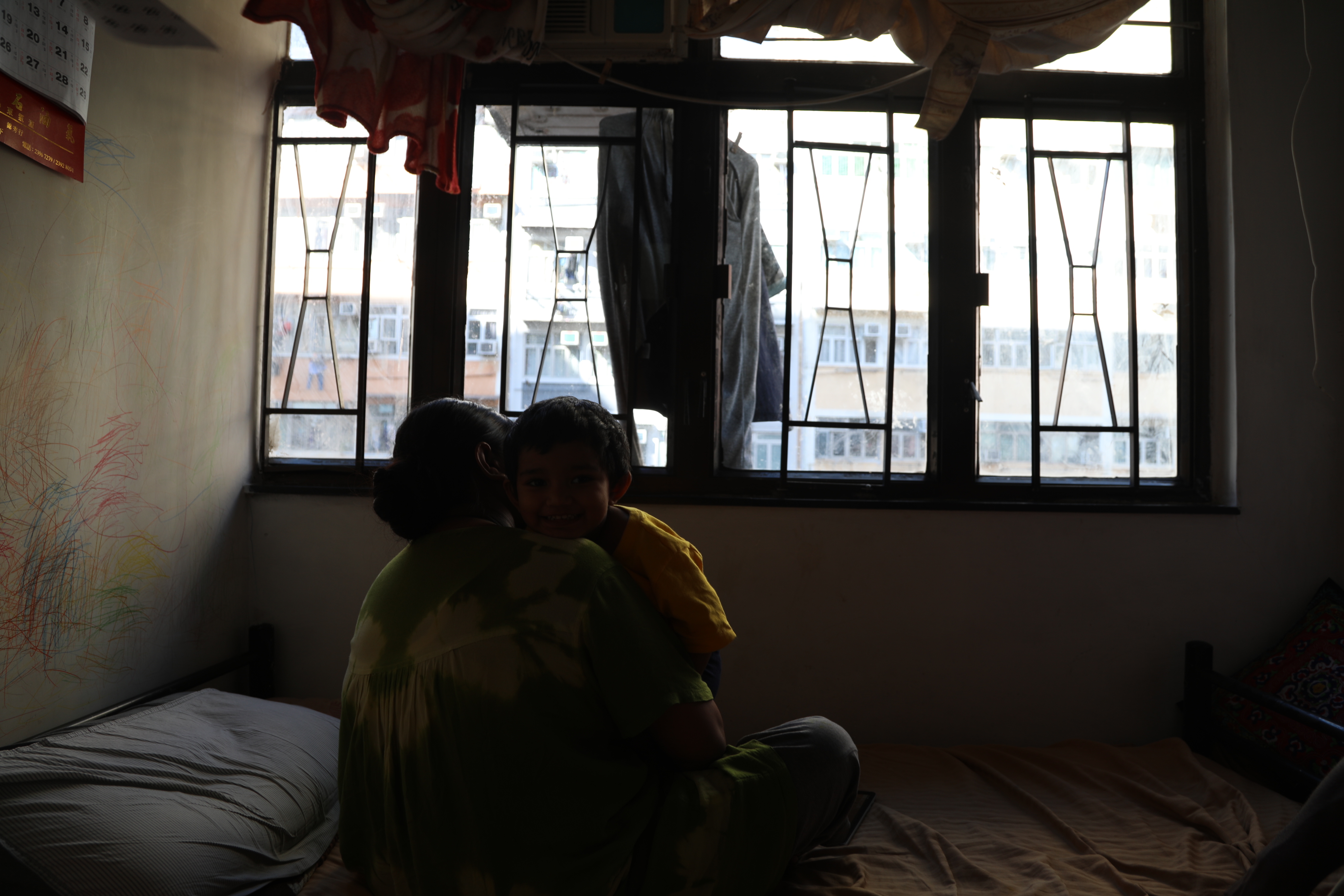 Akter sits with her child on their bed in the family’s small apartment
