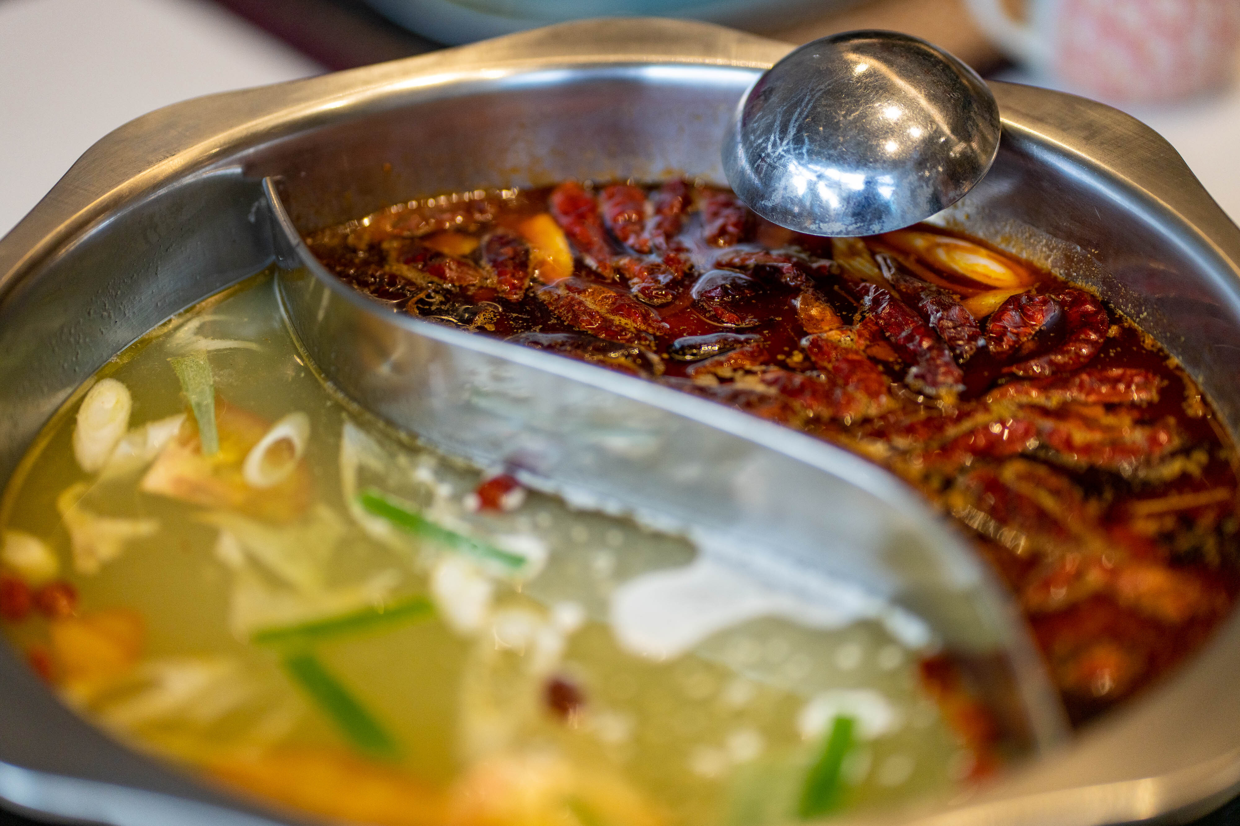 close view of the hotpot, one side is spicy, with chillis and peppers floating in the red broth, while the other is mild with veggies on a clear broth