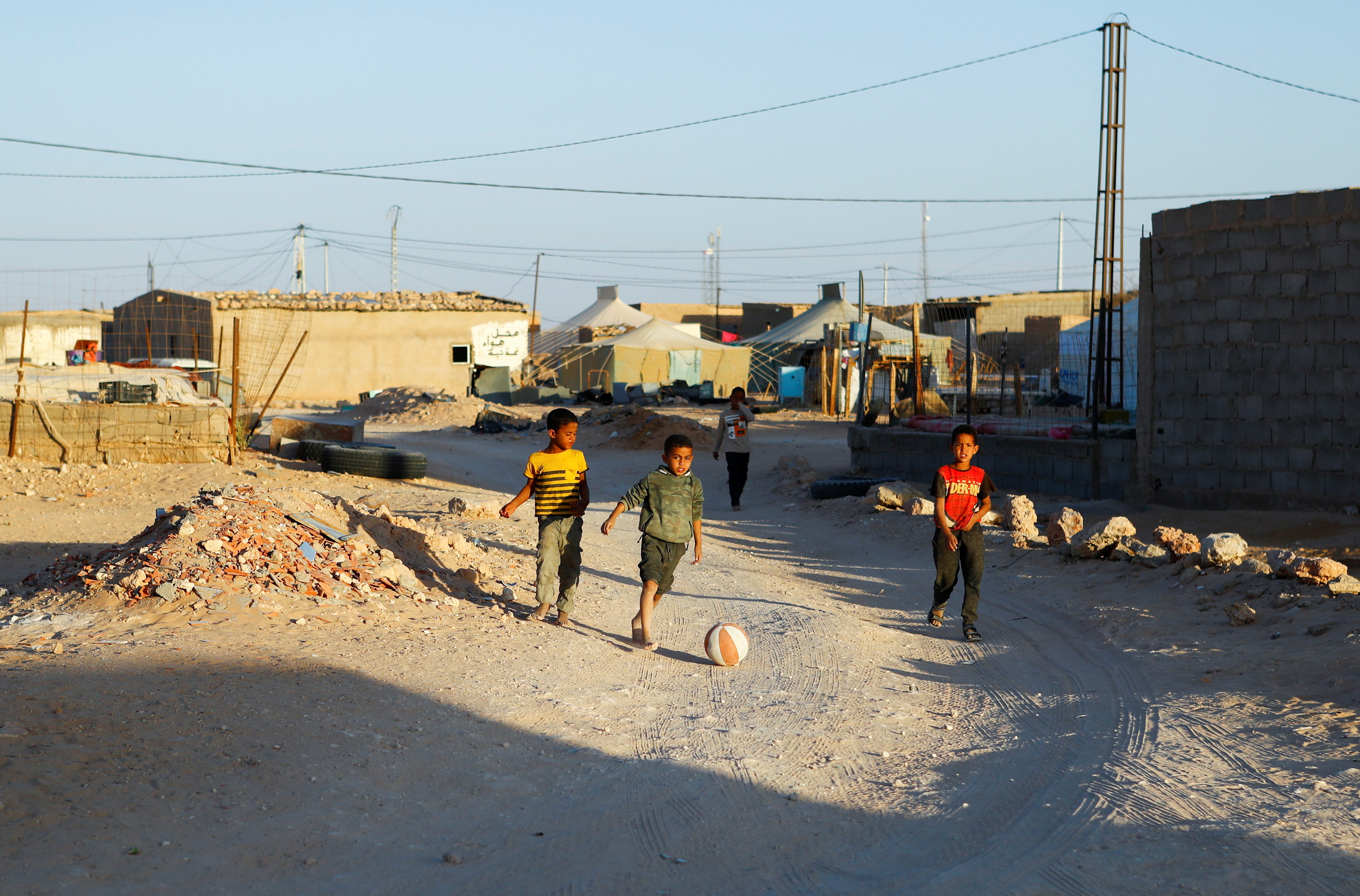 Three boys play football on a road