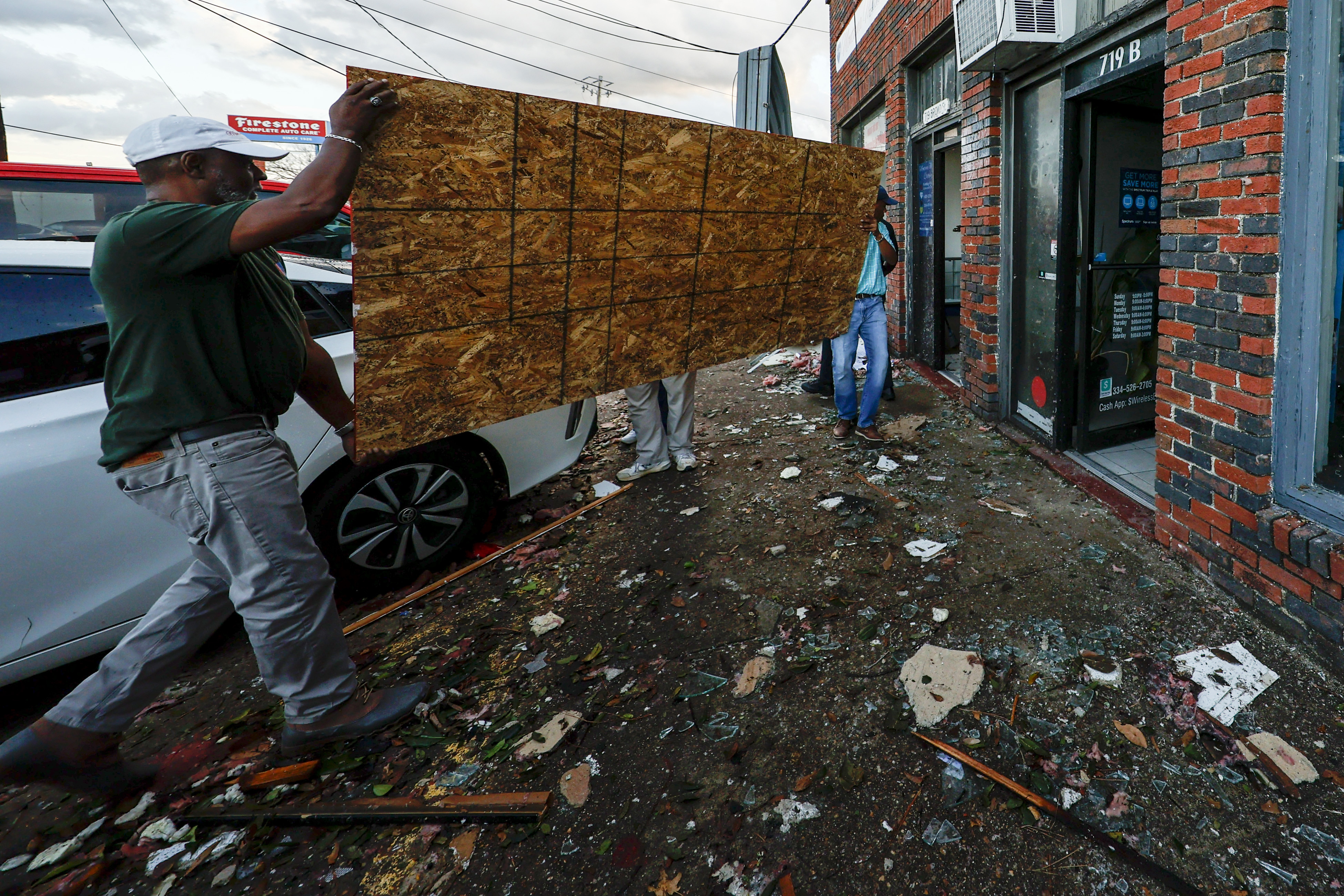 Two men carry a piece of plywood to board up a business