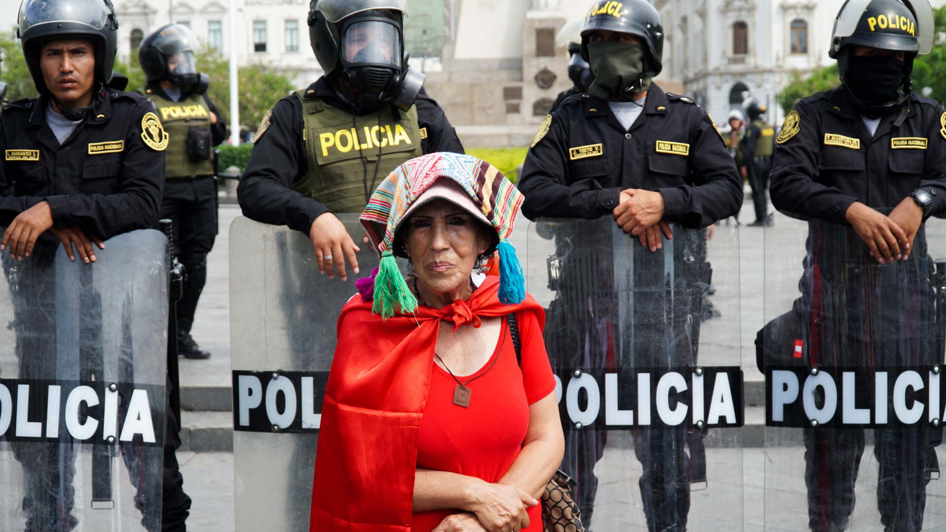 A woman stands before a wall of riot police in central Lima, Peru.