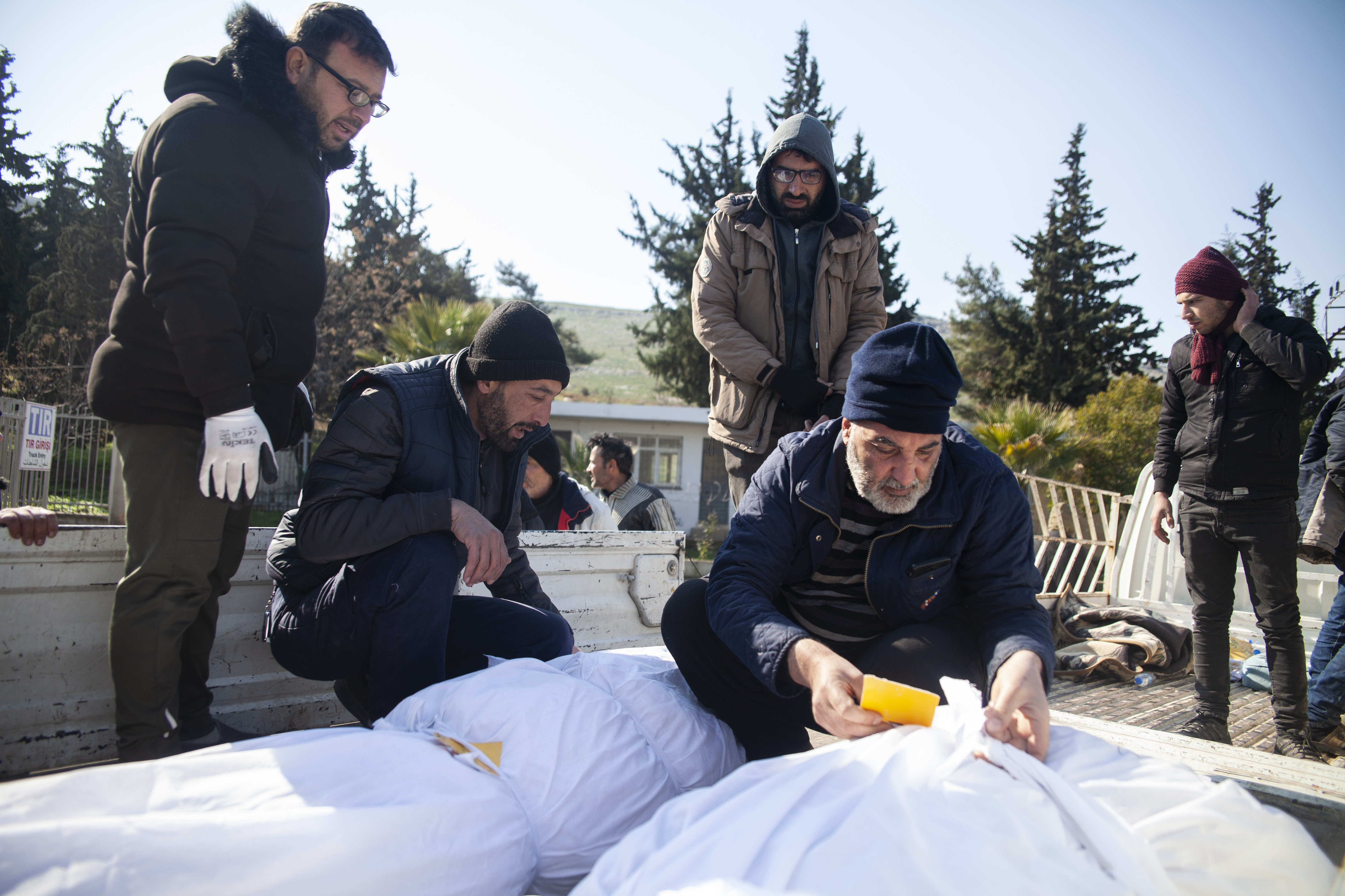 Men on a truck checking the name tags on shrouded bodies