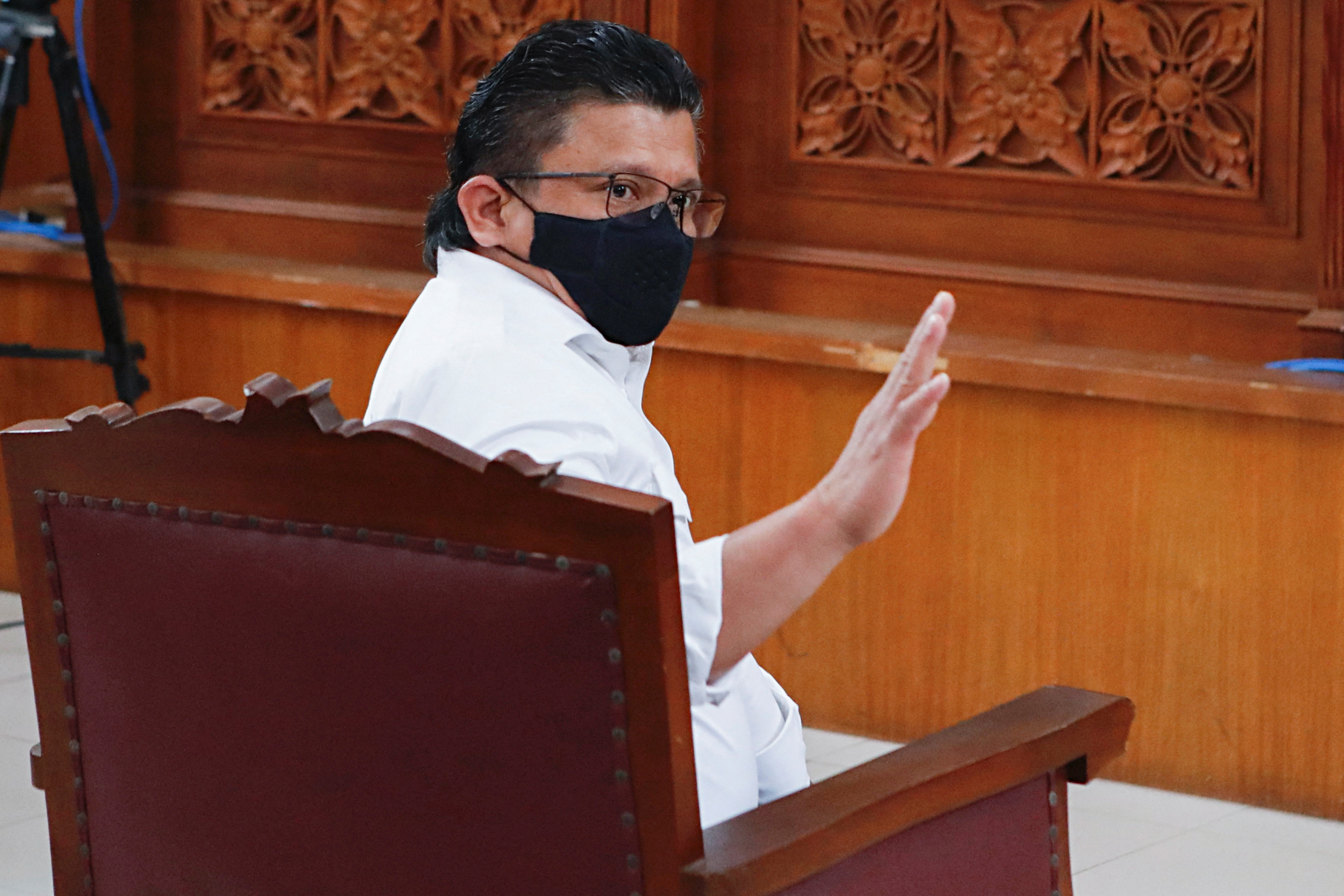 Ferdy Sambo seated in court. He is wearing a white shirt and black facemask and has his hand raised.