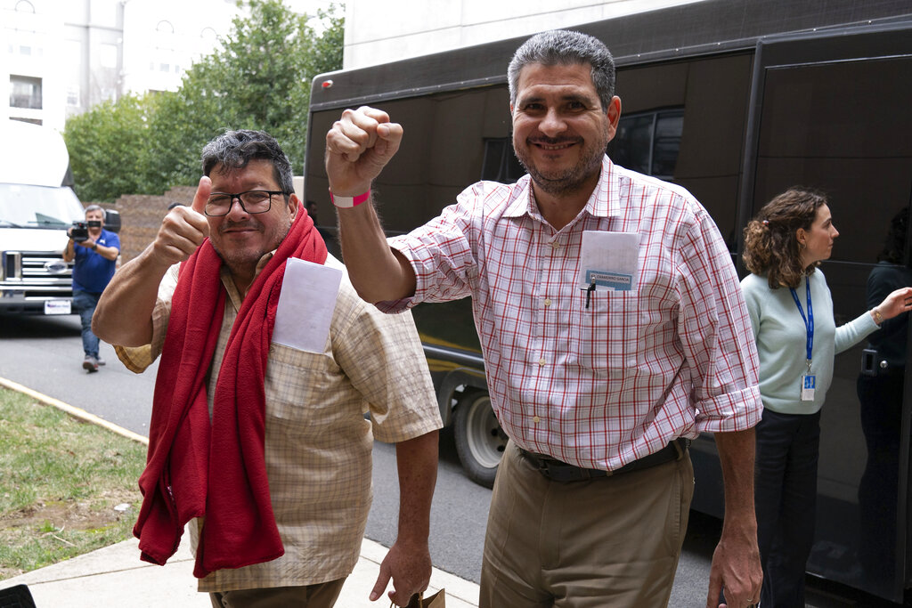 Two men looking at the camera and smiling, one holding a fist in the air and another a thumbs up.