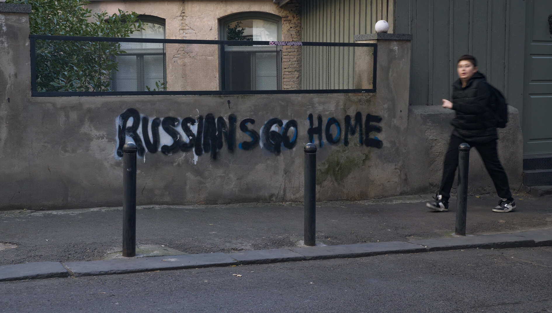 A photo of a boy waling past graffiti on the wall that reads “Russians Go Home".