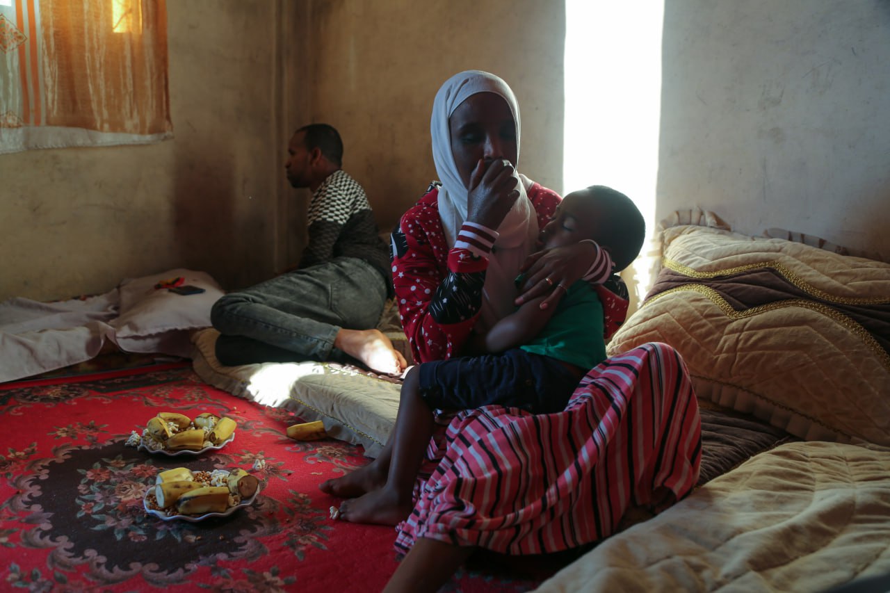 A photo of a woman holding her sleeping son and her husband is laying on the opposite side, behind her.