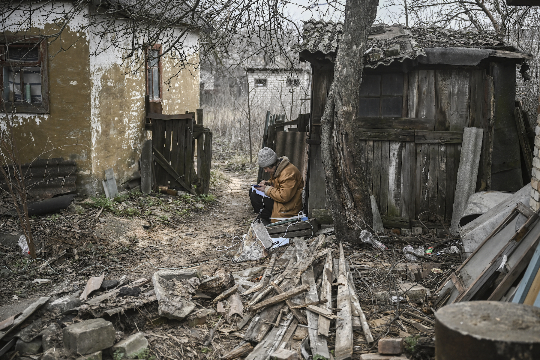 A woman keeps notes and uses her smartphone as she sits in house yard in the town of Chasiv Yar, near Bakhmut, Ukraine.