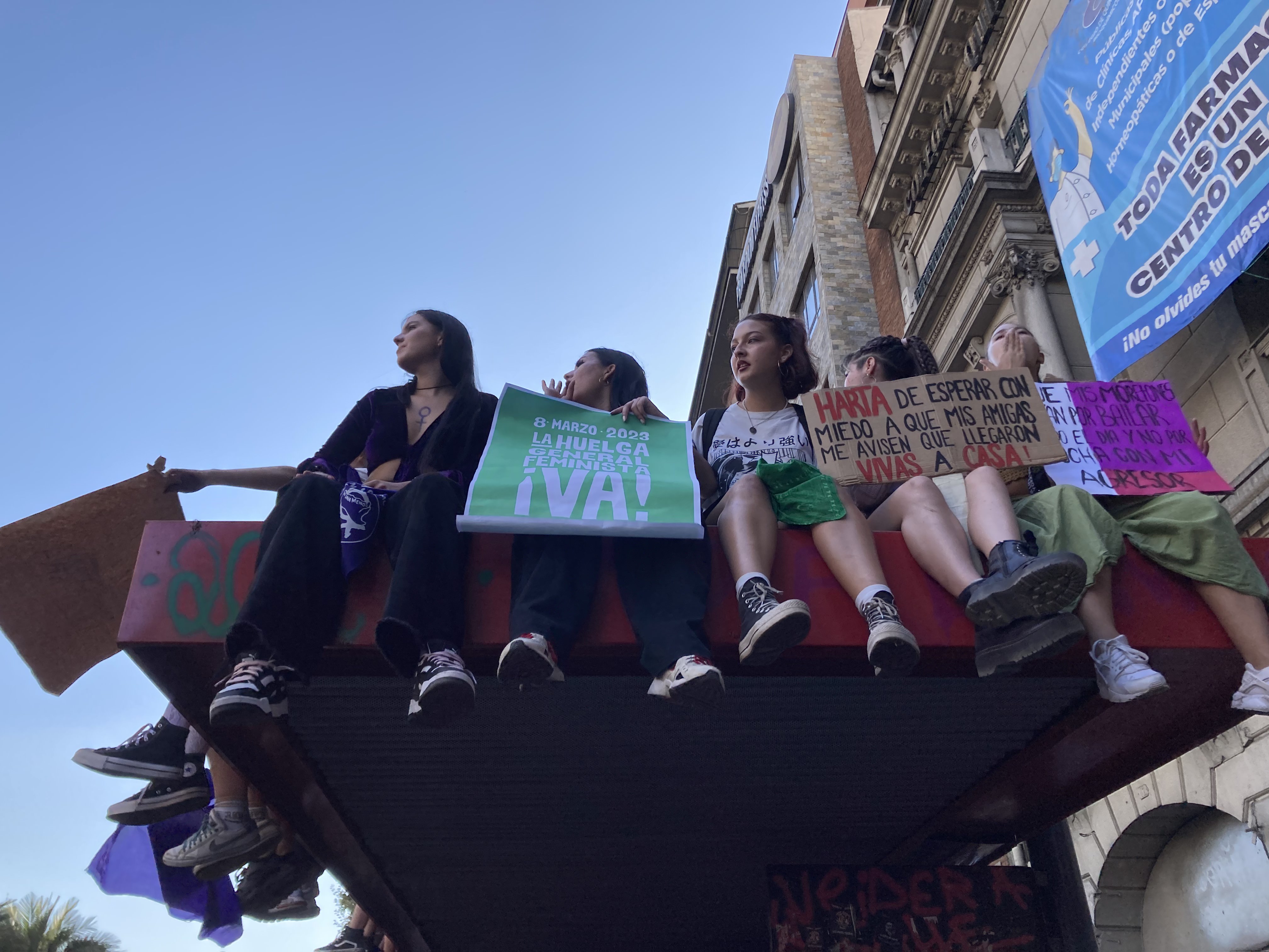 Demonstrators hold signs at a rally while sitting on the edge of a building