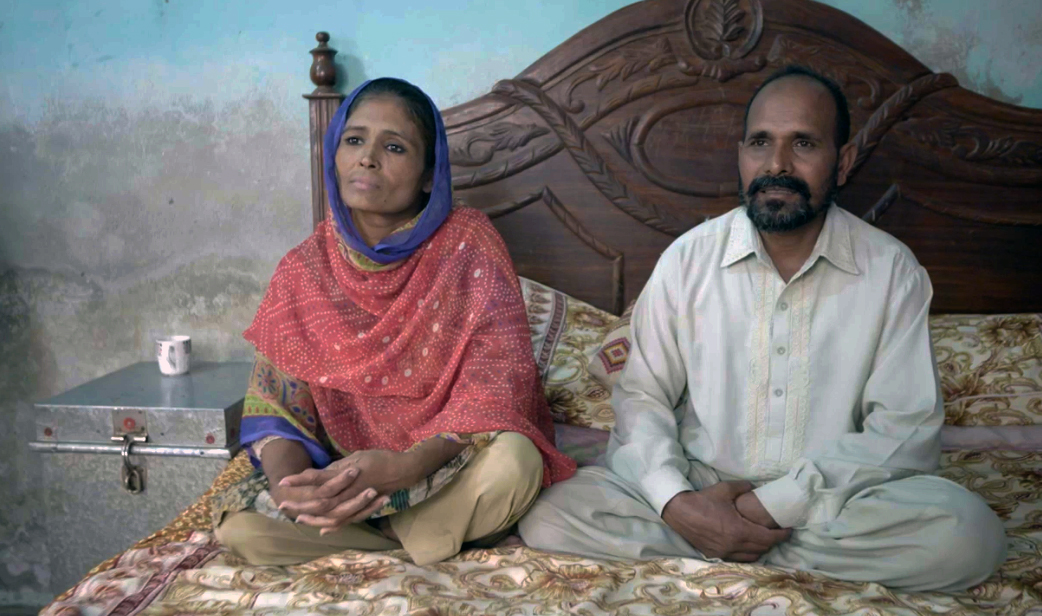 A photo of two people sitting next to each other on a bed.